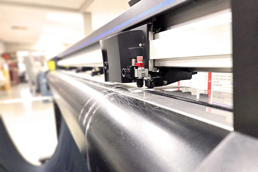Close-up of a large-format printer printing on a wide roll of material in a bright, industrial workspace.