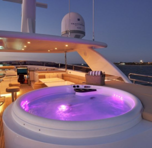 Luxury yacht deck with hot tub and lounge area at sunset.