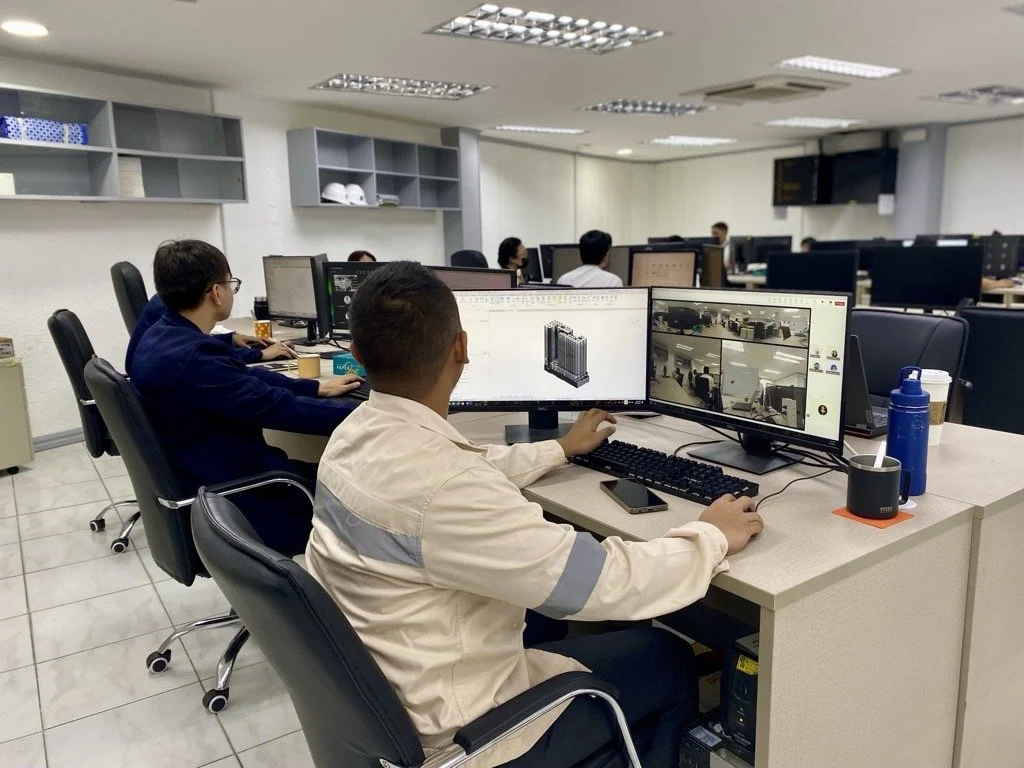 Office with people working on computers, some displaying technical software and a video conferencing call.