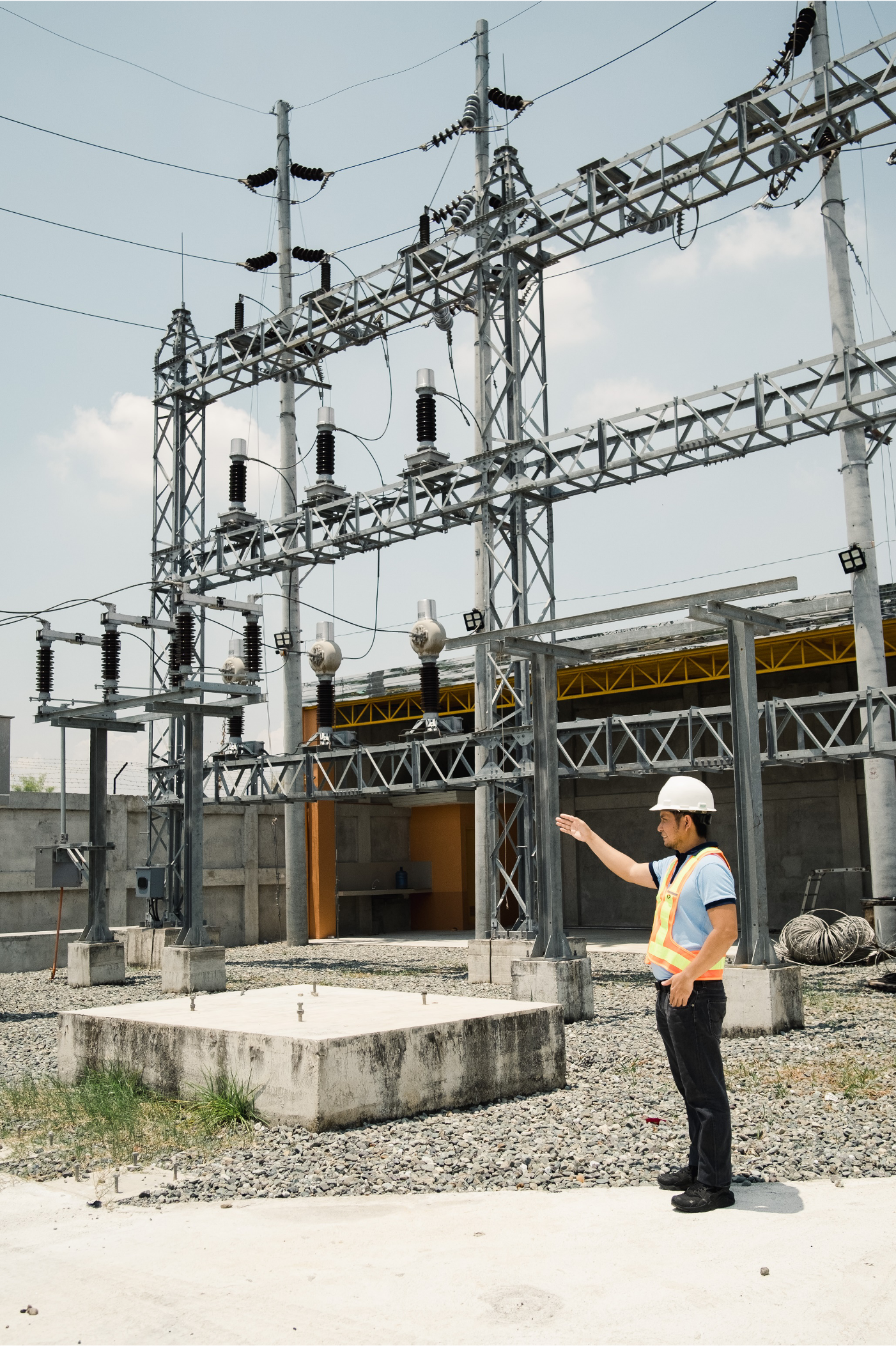 Engineer wearing safety gear inspecting an electrical substation with high-voltage equipment.