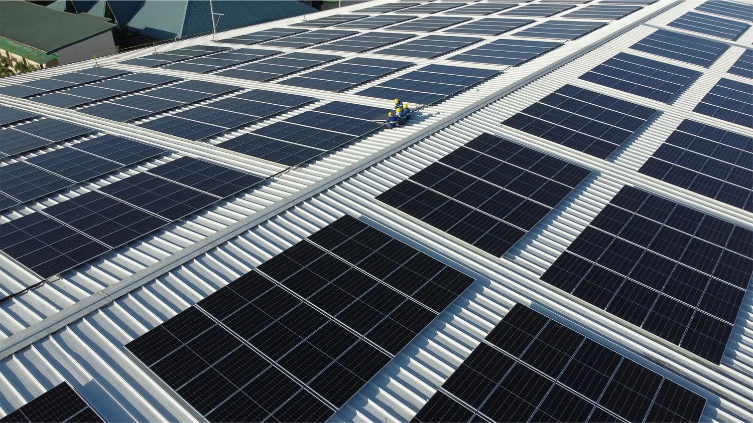 Rooftop with large solar panel array and workers installing panels.