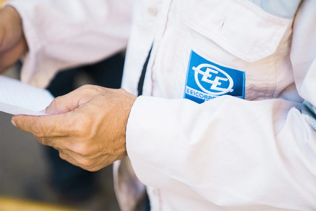 Person in white work jacket reading a document, with a blue EE Corporation logo on the chest.