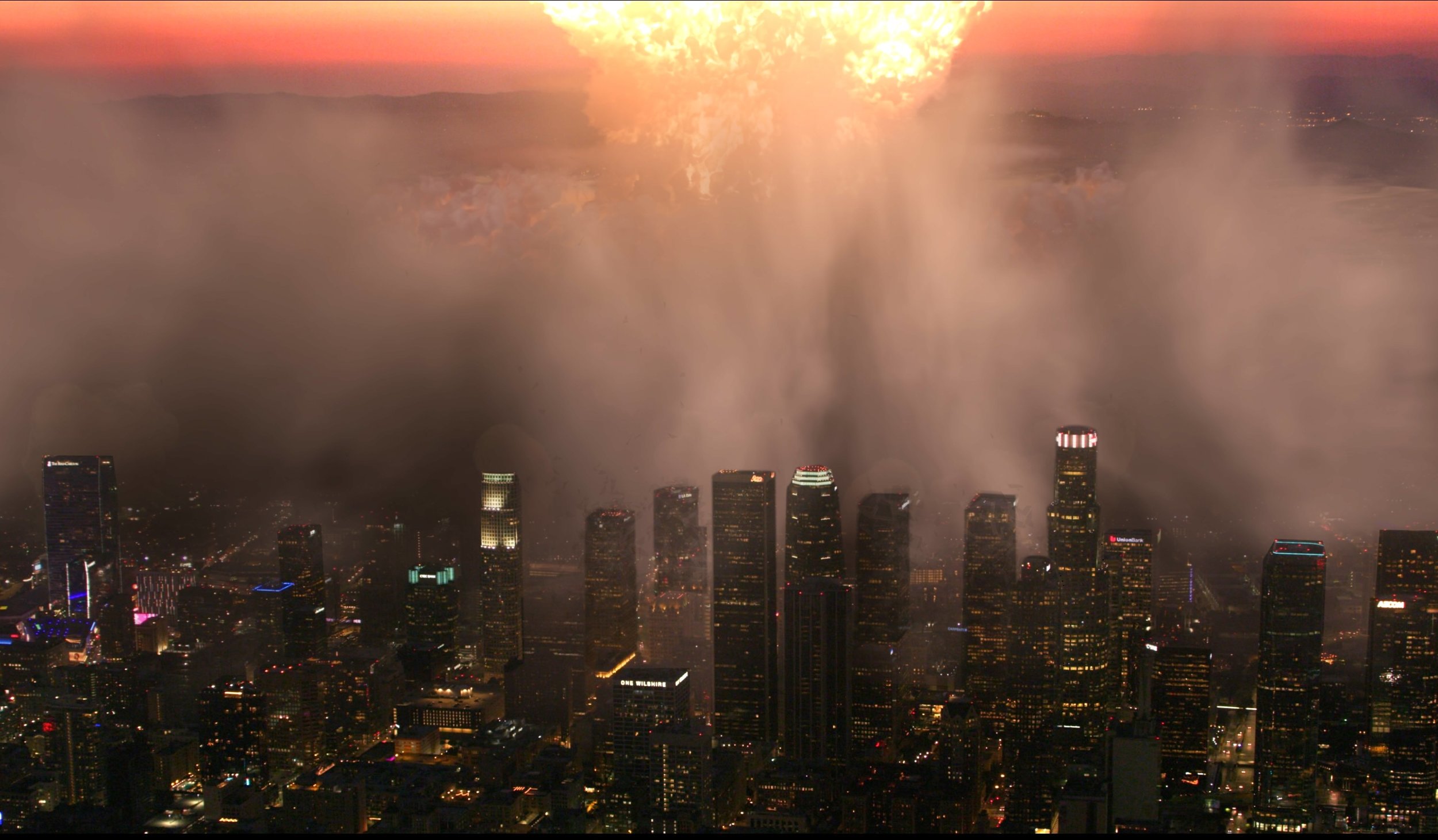 City skyline at night with tall buildings and a large cloud or fog covering parts of the city, illuminated by streetlights and building lights, with an overcast sky.