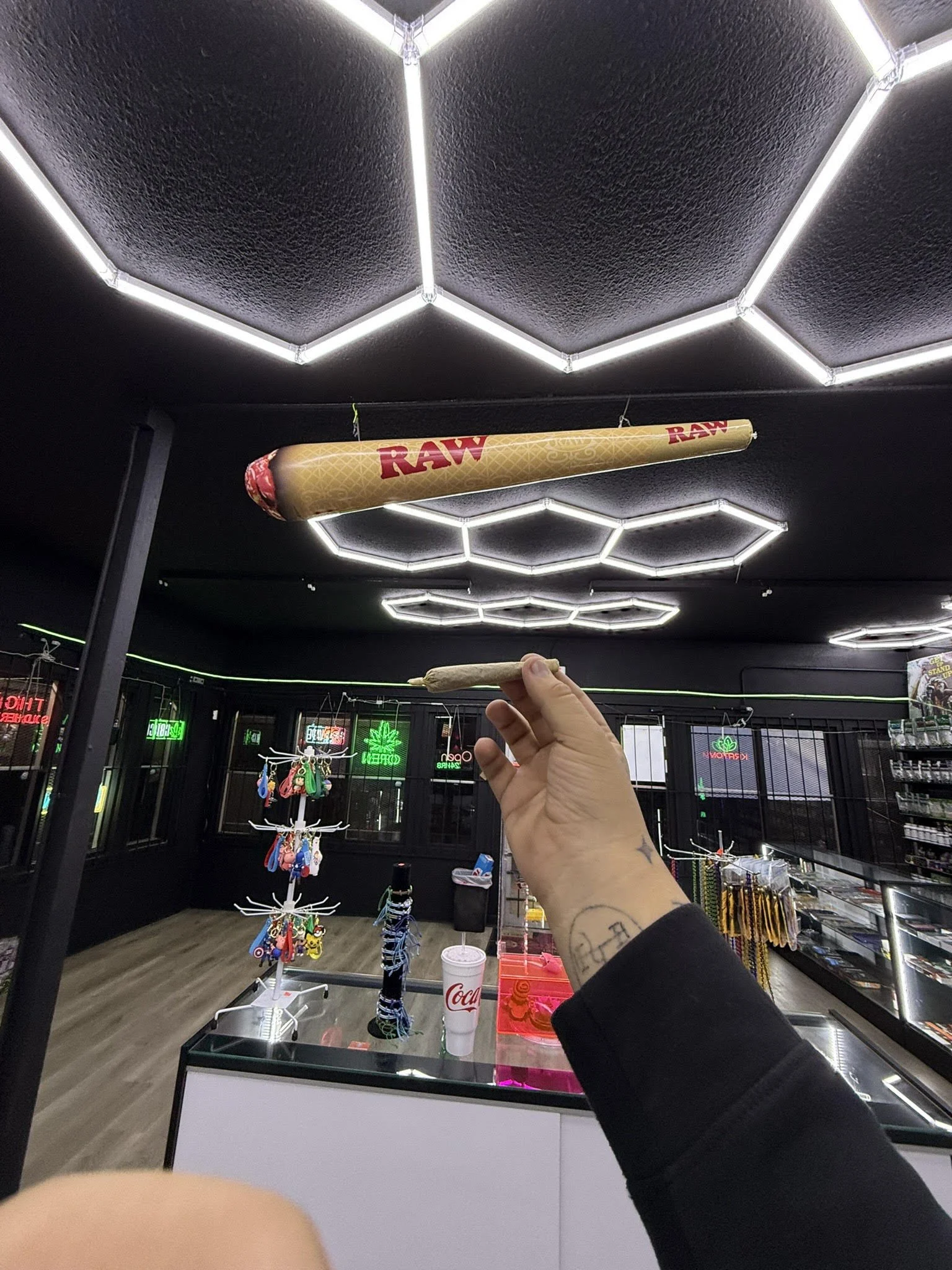 Interior of a smoke shop with a hand holding a rolled item, and large RAW cone decor on the ceiling.
