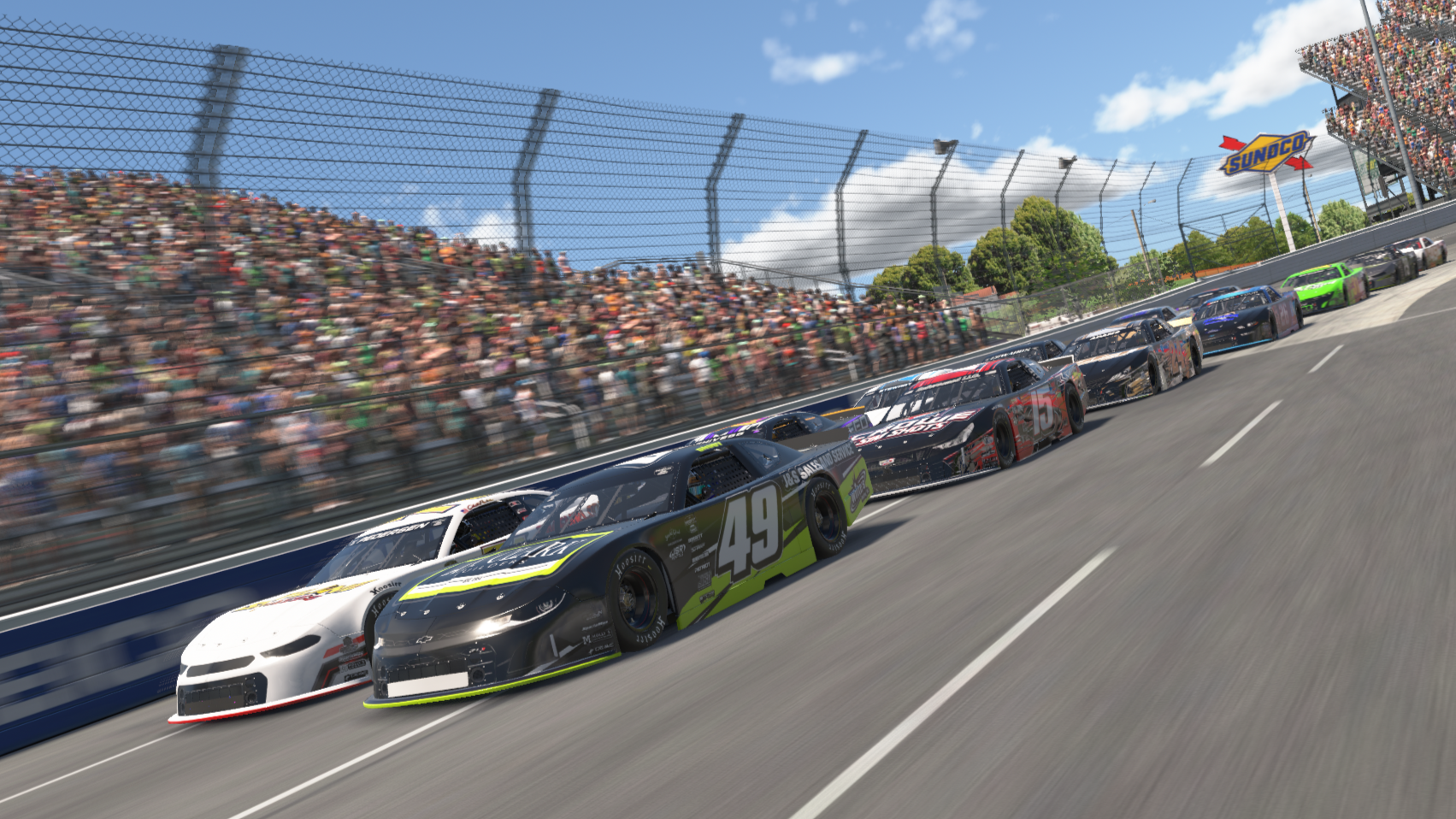 A NASCAR race with multiple cars in a close competition on the track, spectators in the stands, and a Sunoco sign in the background.