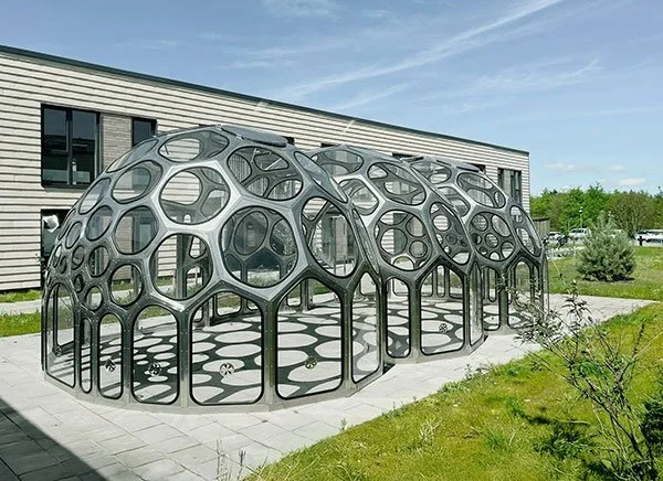 En Njord kuppel og uderum foran en bygning og omgivet af græs og en moderne bygning i baggrunden.