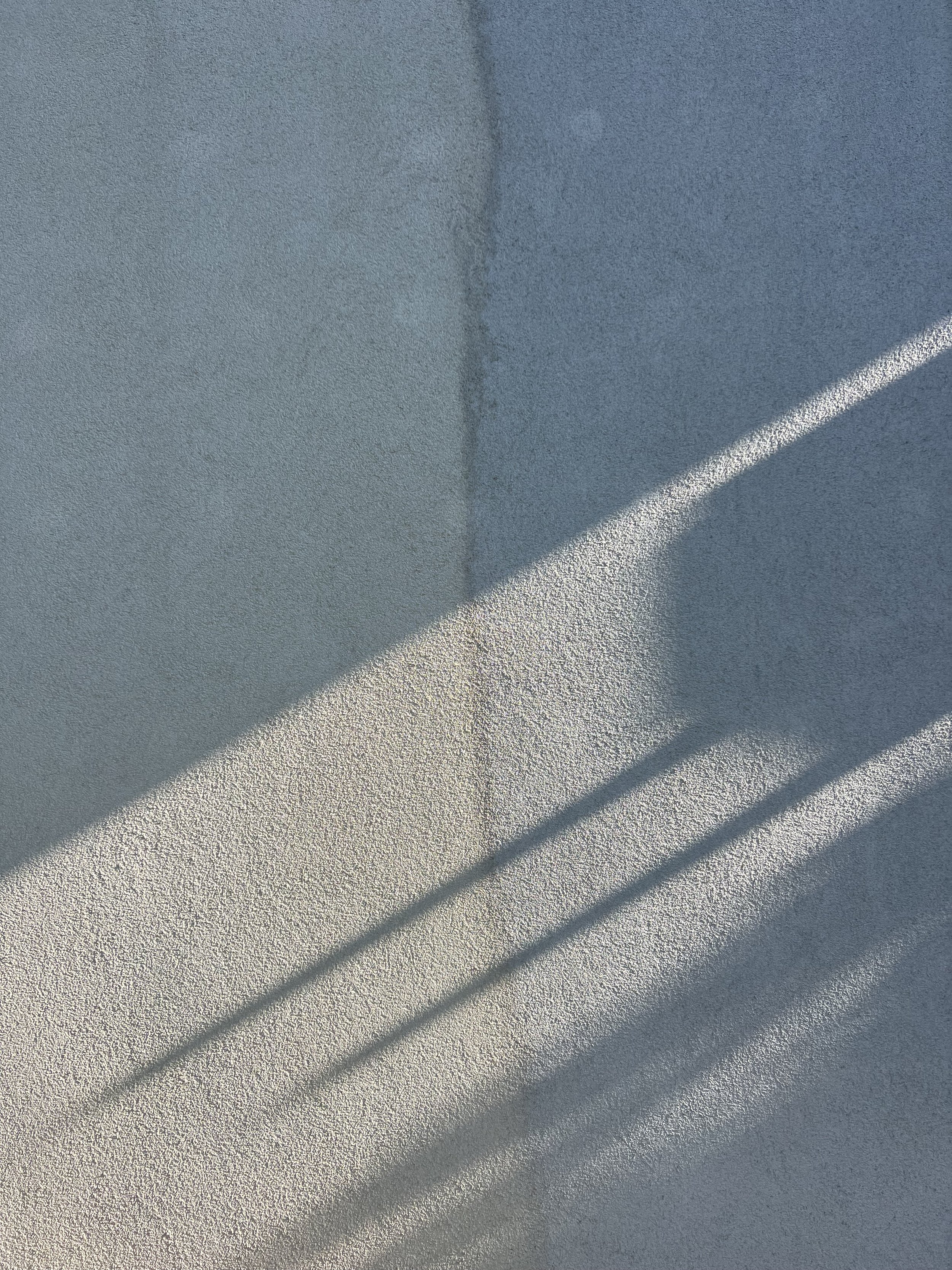 Sunlight casting diagonal shadows on a textured wall.