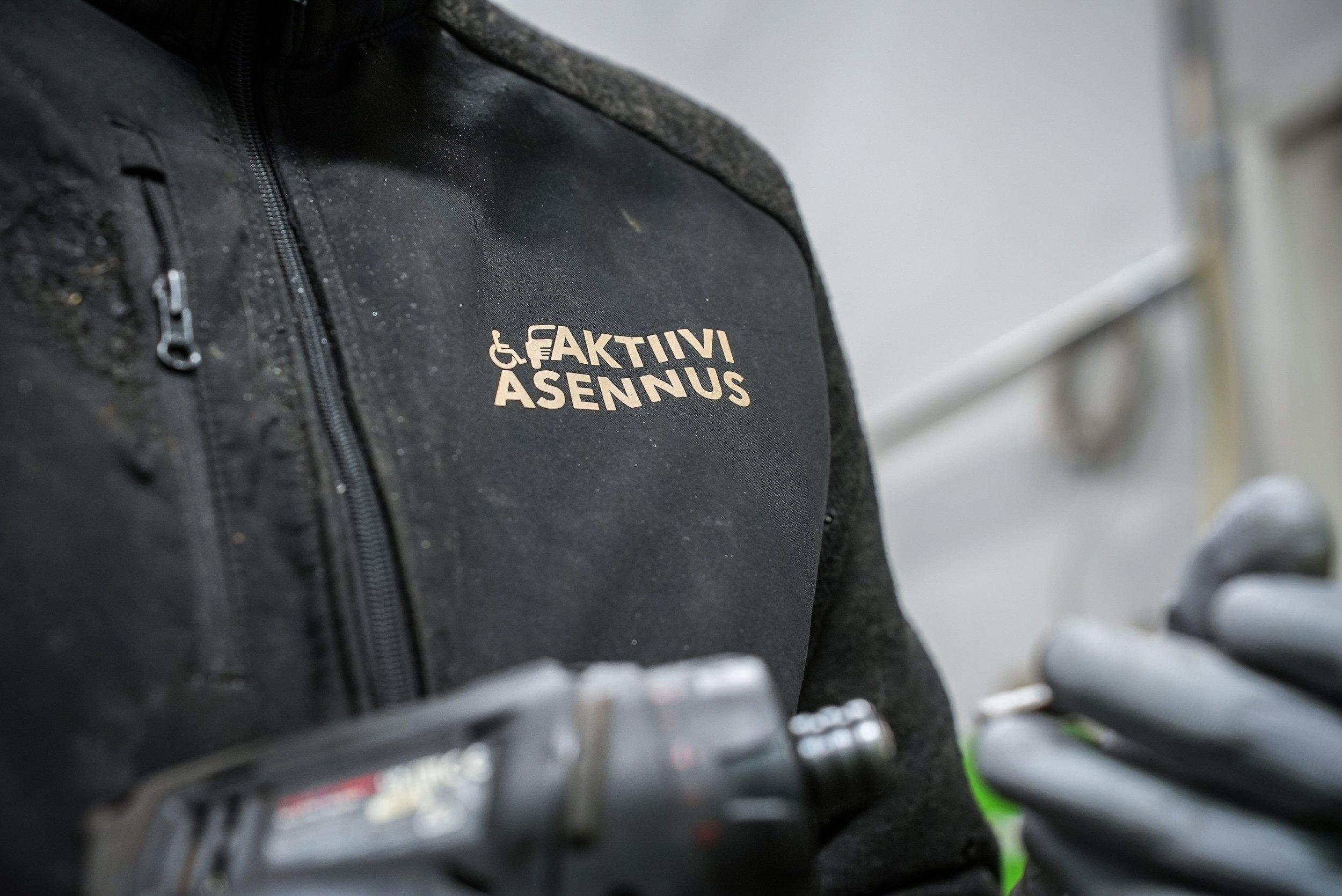 Henkilön mustassa takissa on teksti "AKTIVI ASENNUS" ja käsin tekee jotakin korjausta.