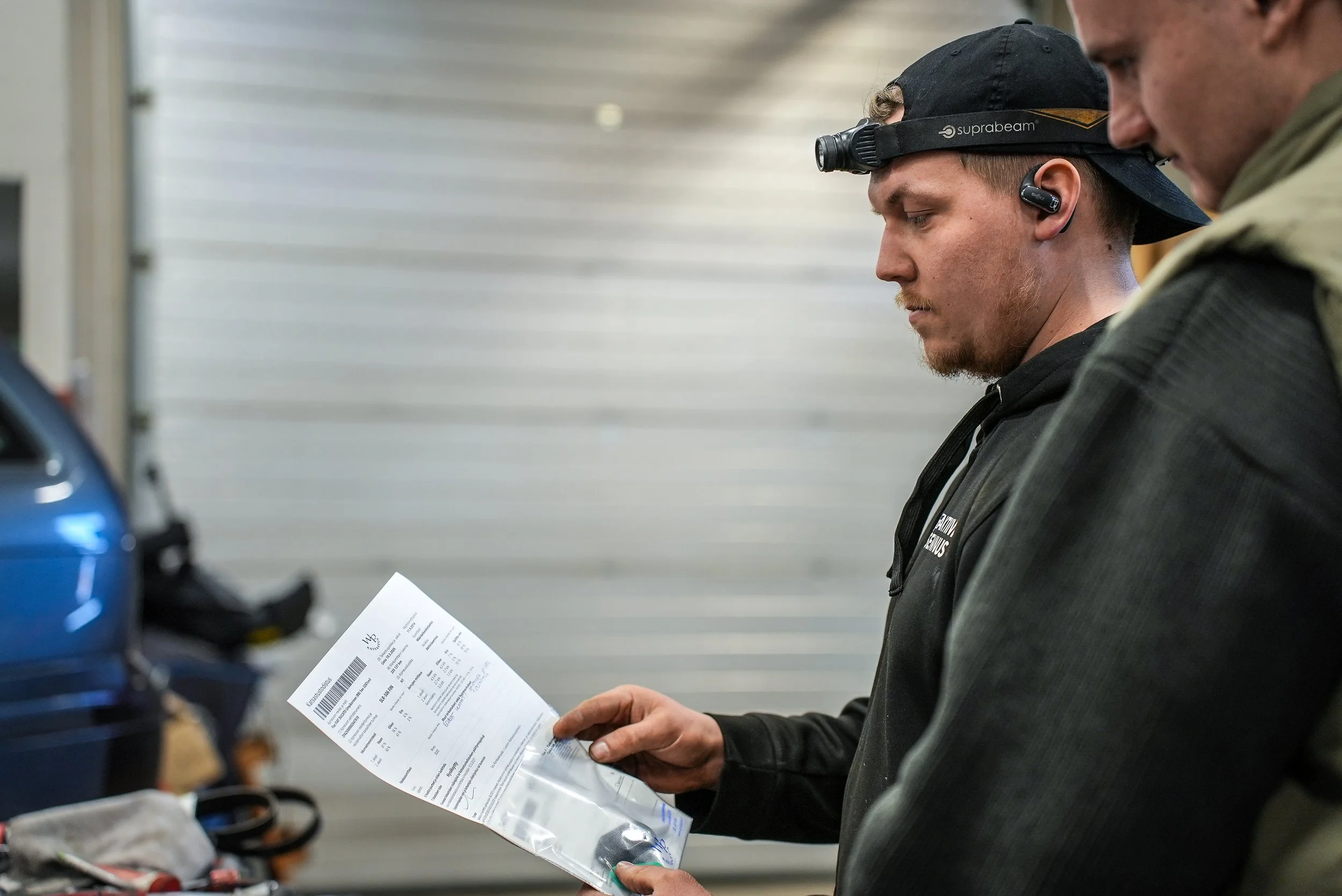 Kaksi miestä katselee katsastuslappua tai matkustusasiakirjaa sisätiloissa.