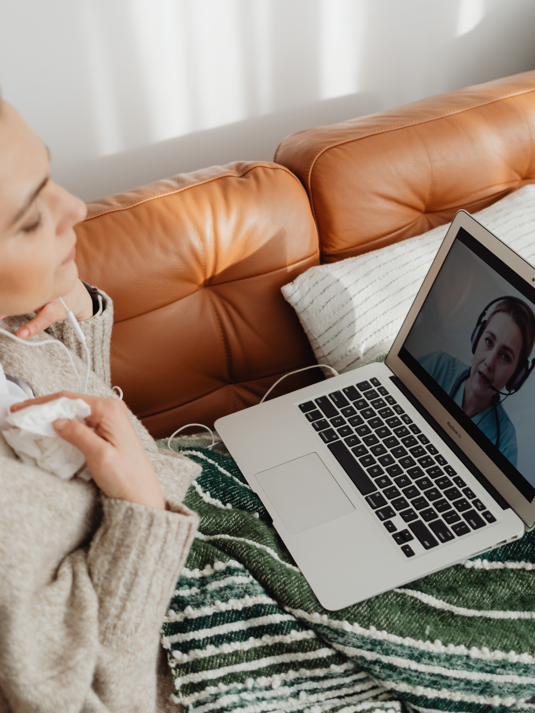 A woman sitting on a couch with a blanket, participating in a video call with a woman wearing a headset on a laptop. Image used to describe step one in the onboarding process for Socials With Michelle, which involves a consultation call.