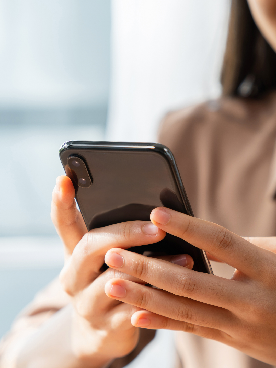 Person holding a smartphone with both hands, focusing on the phone. Image used to describe step two in the onboarding process for Socials With Michelle, which involves information sharing (brand kits etc.)