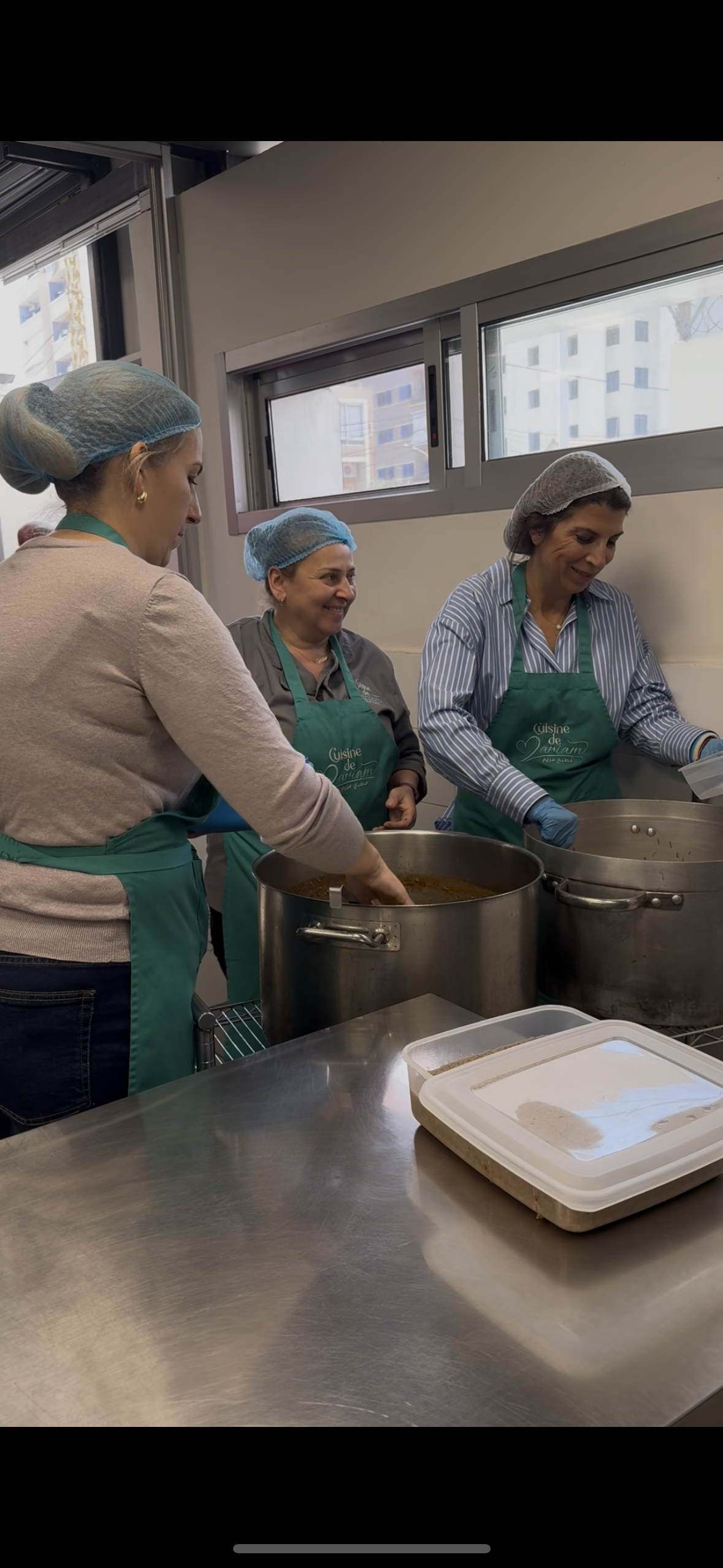 femmes souriantes dans une cuisine en train de préparer un repas dans des grandes casseroles