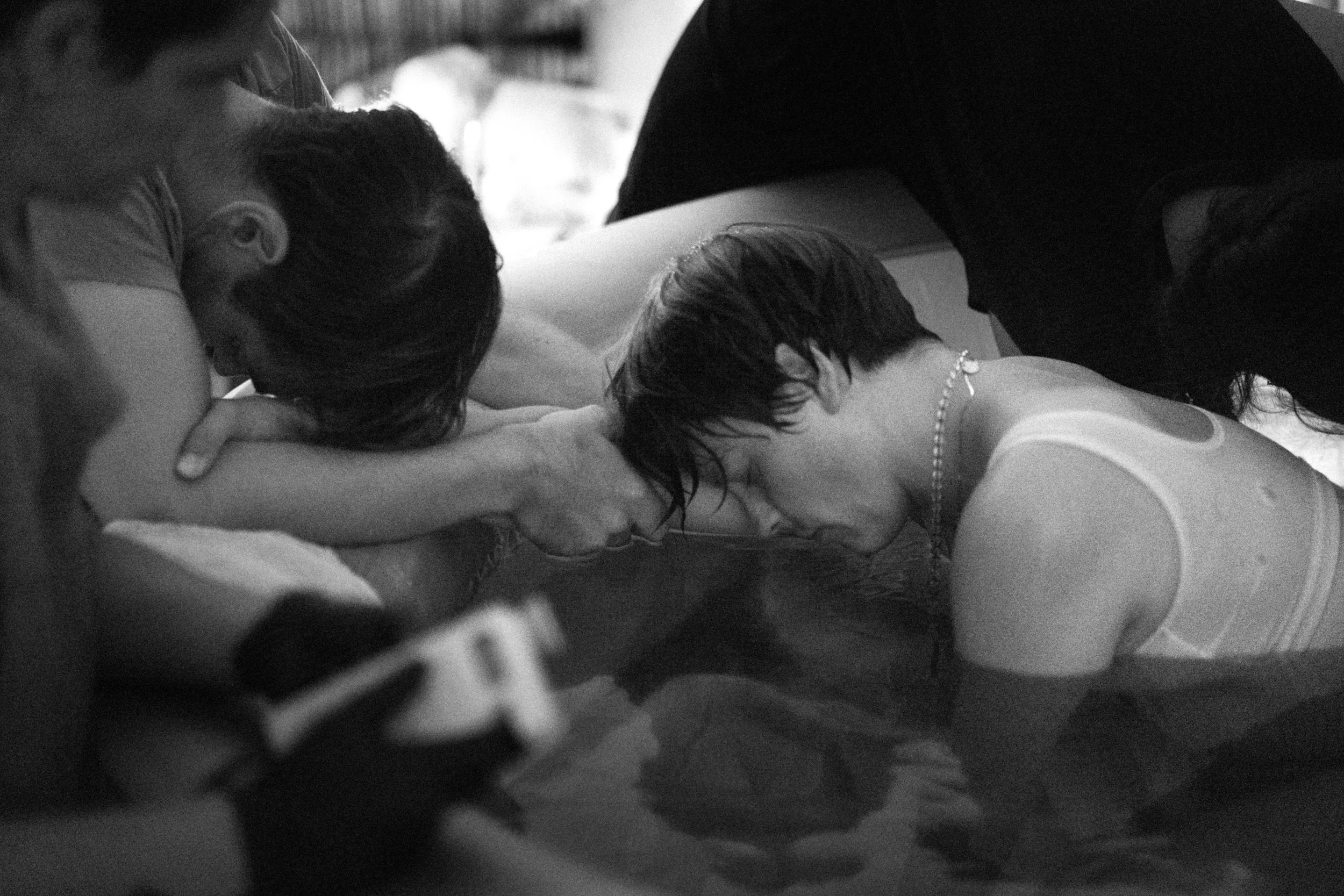People participate in a baptism ceremony, with two individuals submerged in water, heads bowed and eyes closed, engaging in the religious ritual.