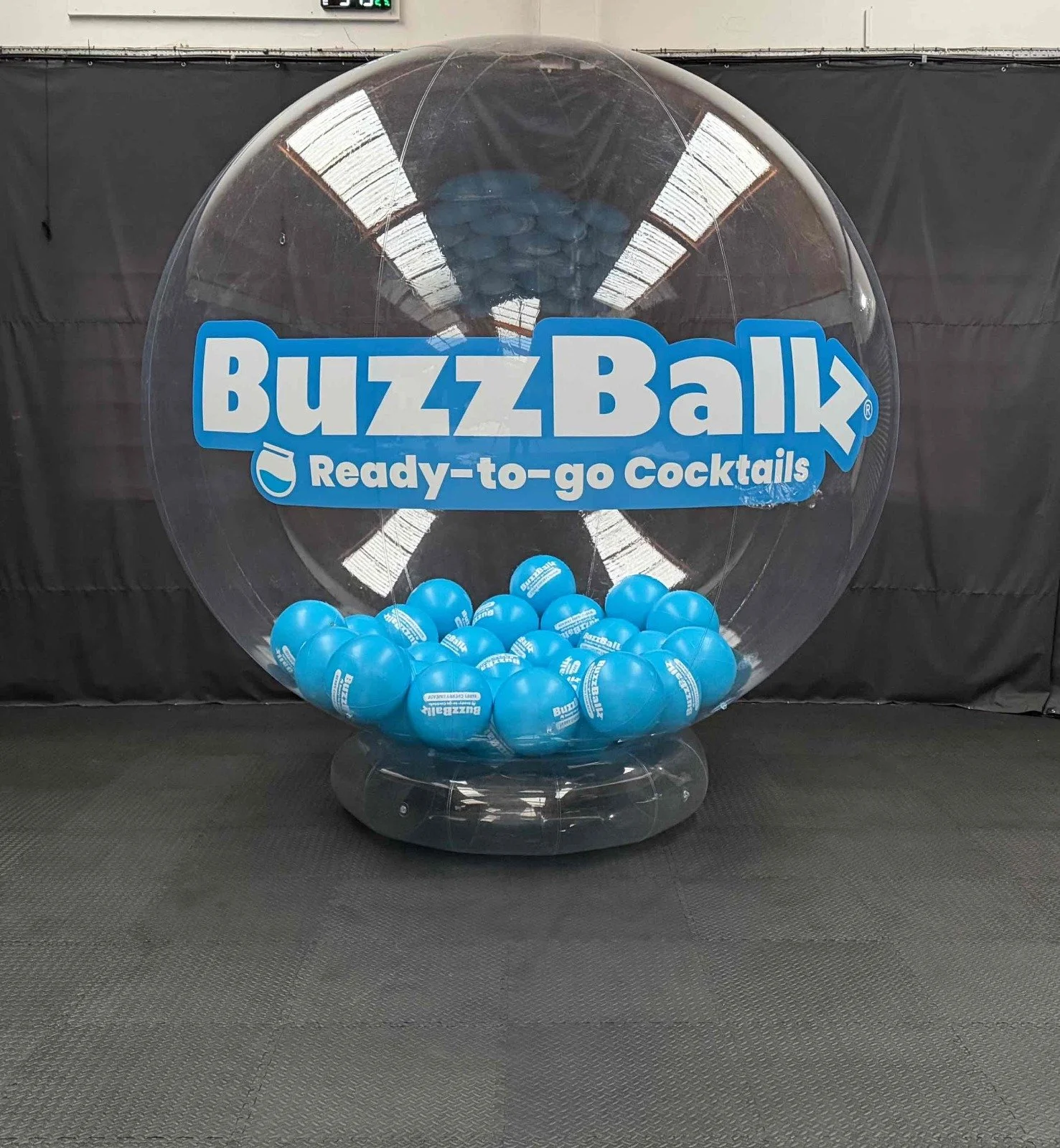 A large transparent plastic ball filled with blue balls, displaying the BuzzBallz logo and the phrase 'Ready-to-go Cocktails'.