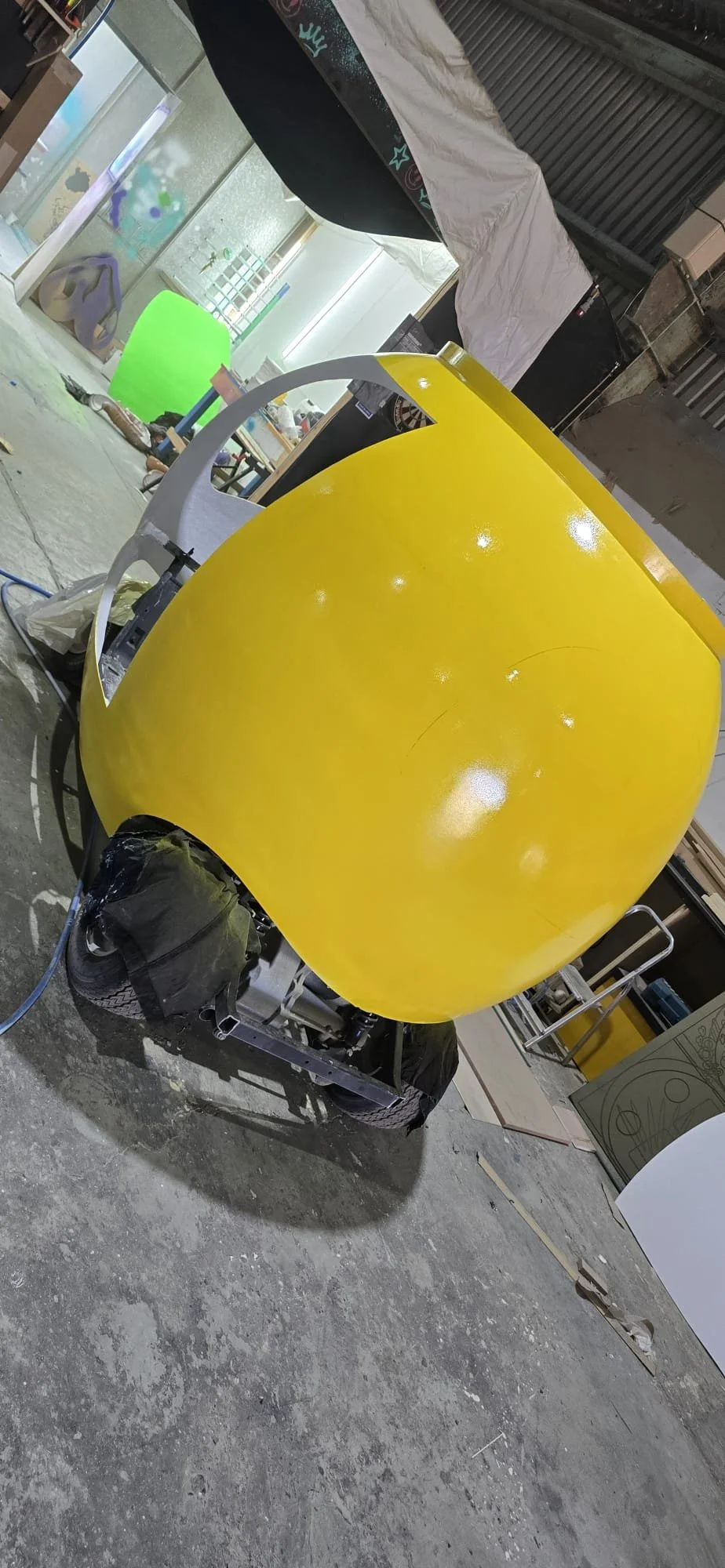Yellow teardrop-shaped vehicle body in a workshop with tools and equipment in the background.