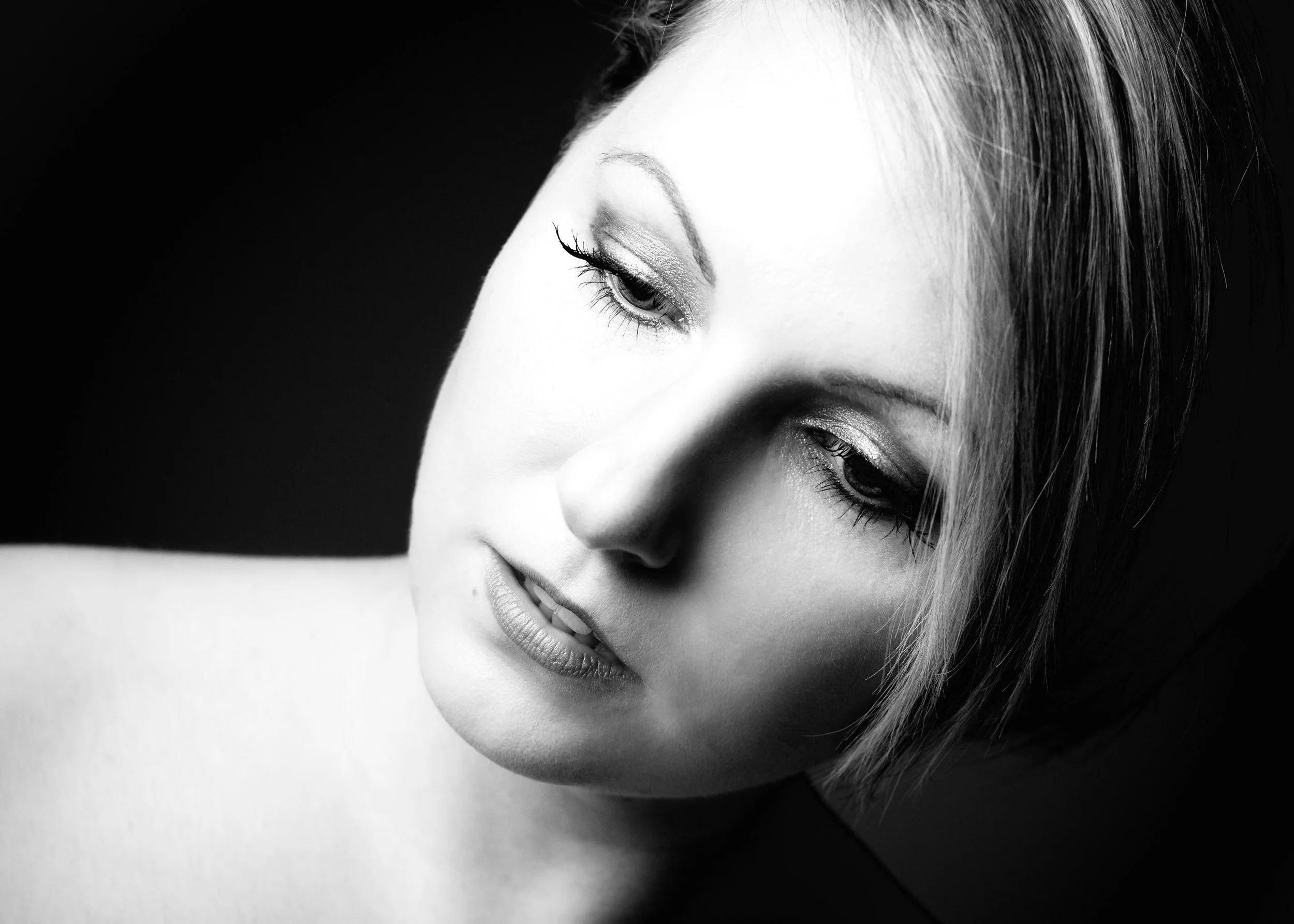 Schwarz-weiß-Porträt einer jungen Frau mit kurzem, glattem Haar, getragen dunkler Lidschatten, Blick nach unten, leichter Köcheröffnung der Lippen.