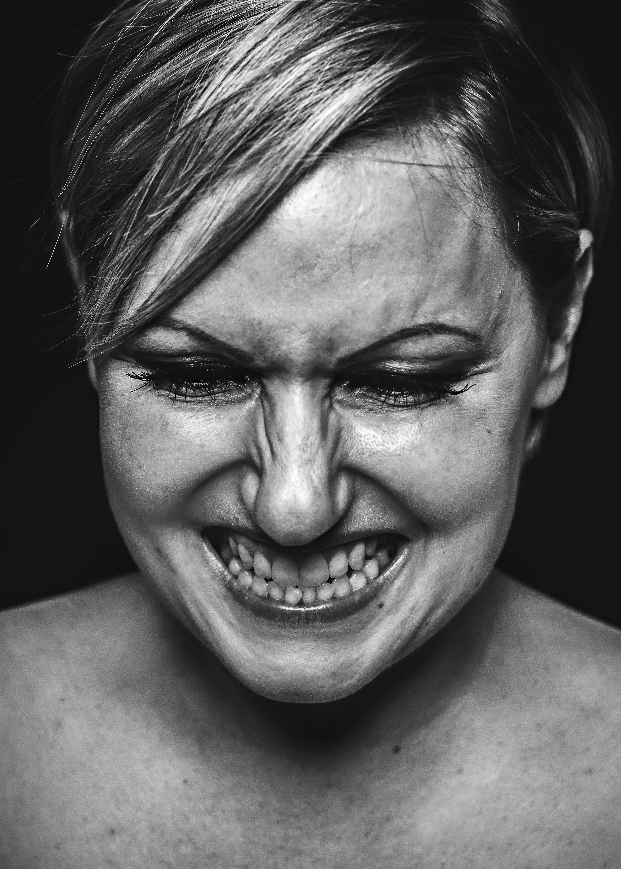 Schwarz-Weiß-Foto eines Mannes mit einem verzerrten, aggressiven Gesichtsausdruck, mit zusammengekniffenen Augen und offenem Mund, das Zähne zeigt.