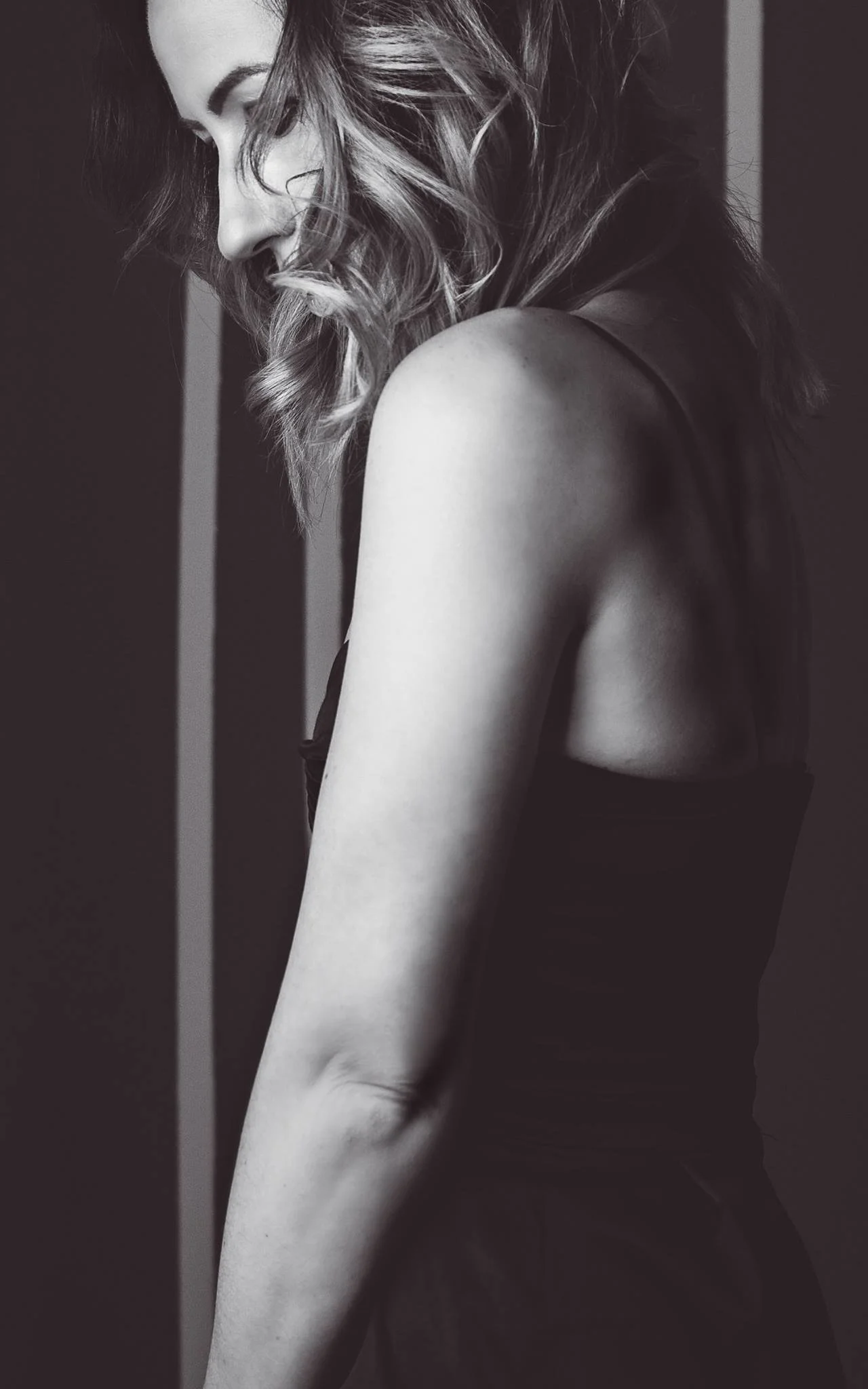 Schwarz-weiß-Fotografie einer jungen Frau mit lockigem Haar, die nach unten schaut, nur der obere Teil ihres Körpers ist sichtbar.