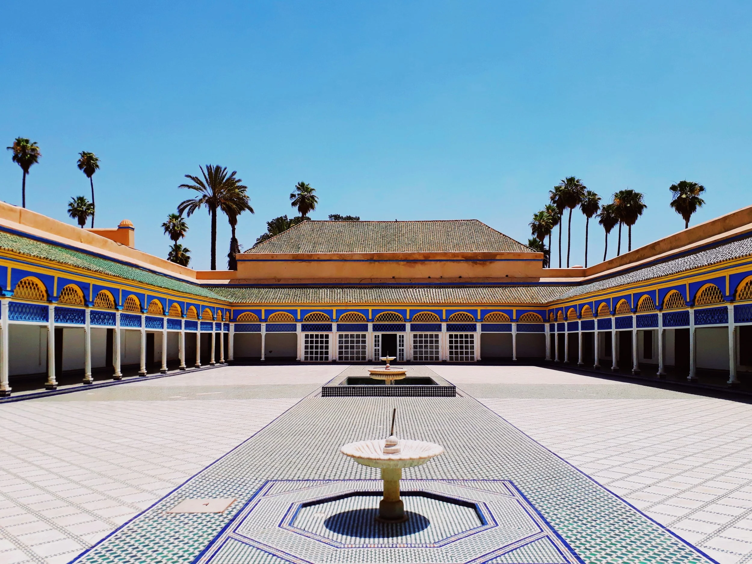 Binnenhof in Den Haag met een open binnenplaats, centrale fontein en kleurrijk betegelde vloer en muren, omgeven door palmbomen en een heldere blauwe hemel.