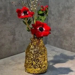 Vase doré contenant des fleurs rouges, blanches et vertes sur une surface grise. Gateaux anniversaire Maison TCHOVI 