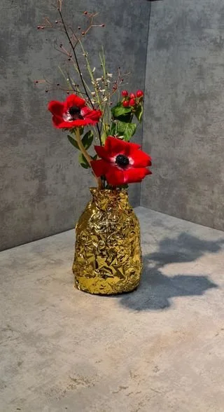 Gateau sur mesure - Maison Tchovi. Un vase doré contenant des fleurs rouges, des branches et des baies rouges sur un fond gris.