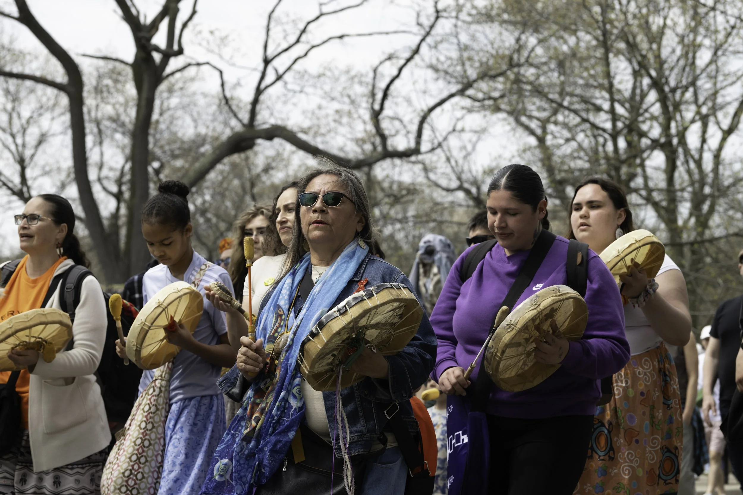 Grandmother Vivien Recollet playing a hand drum with a group of drummers