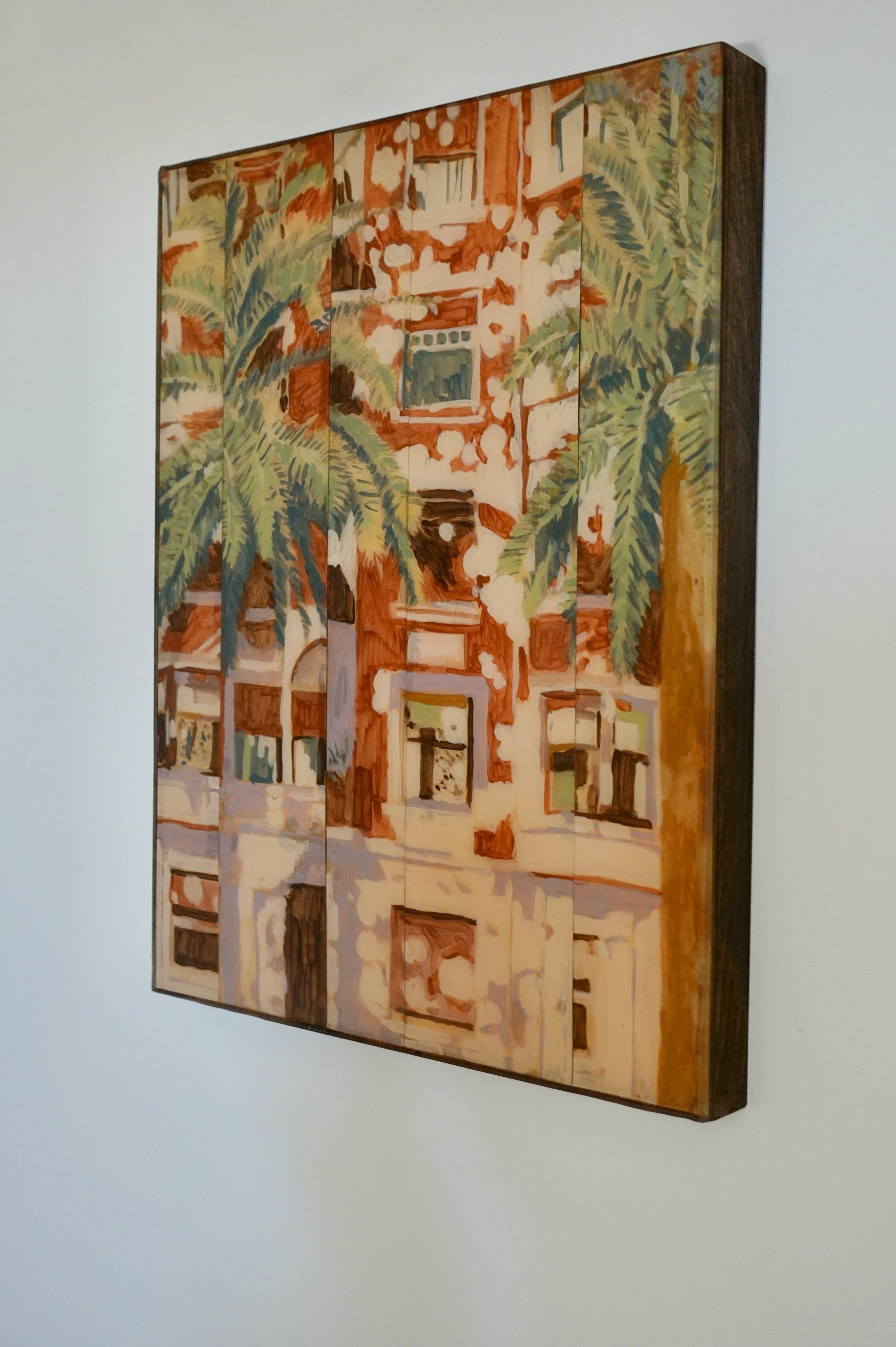 An artwork on a wall depicting a building with large fronds of palm trees in the foreground, painted in warm tones.