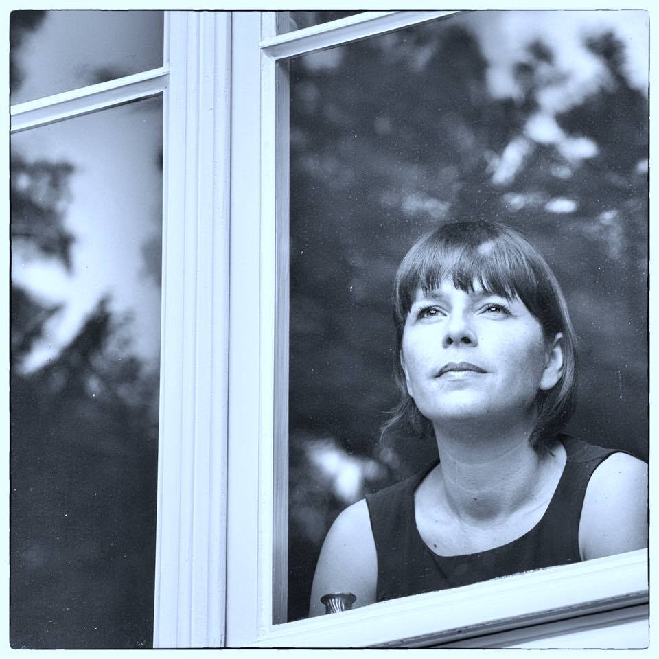 A woman with short dark hair looking out of a window.