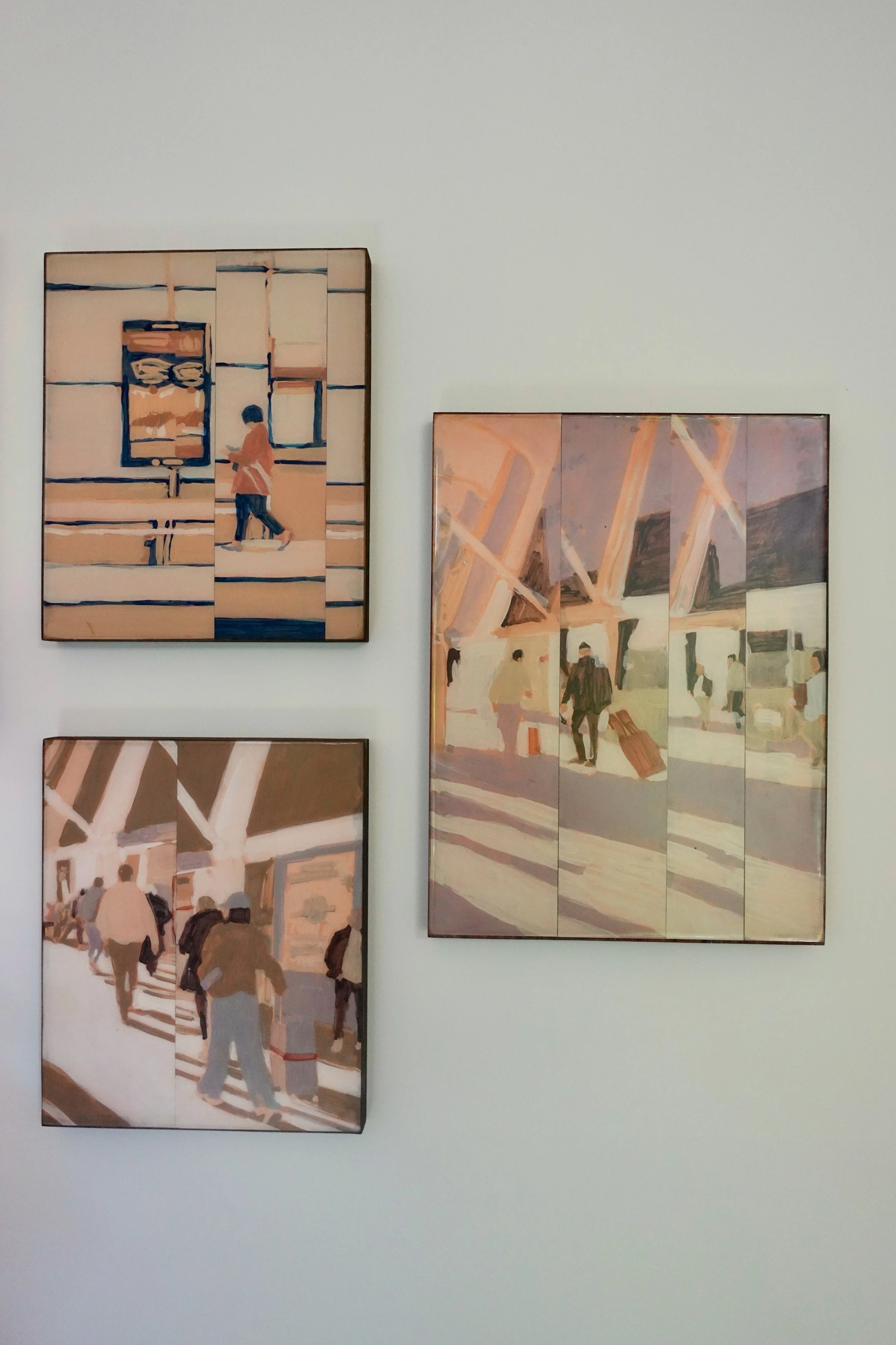 Three paintings on a display wall depicting people in an airport terminal with large windows and steel structures.