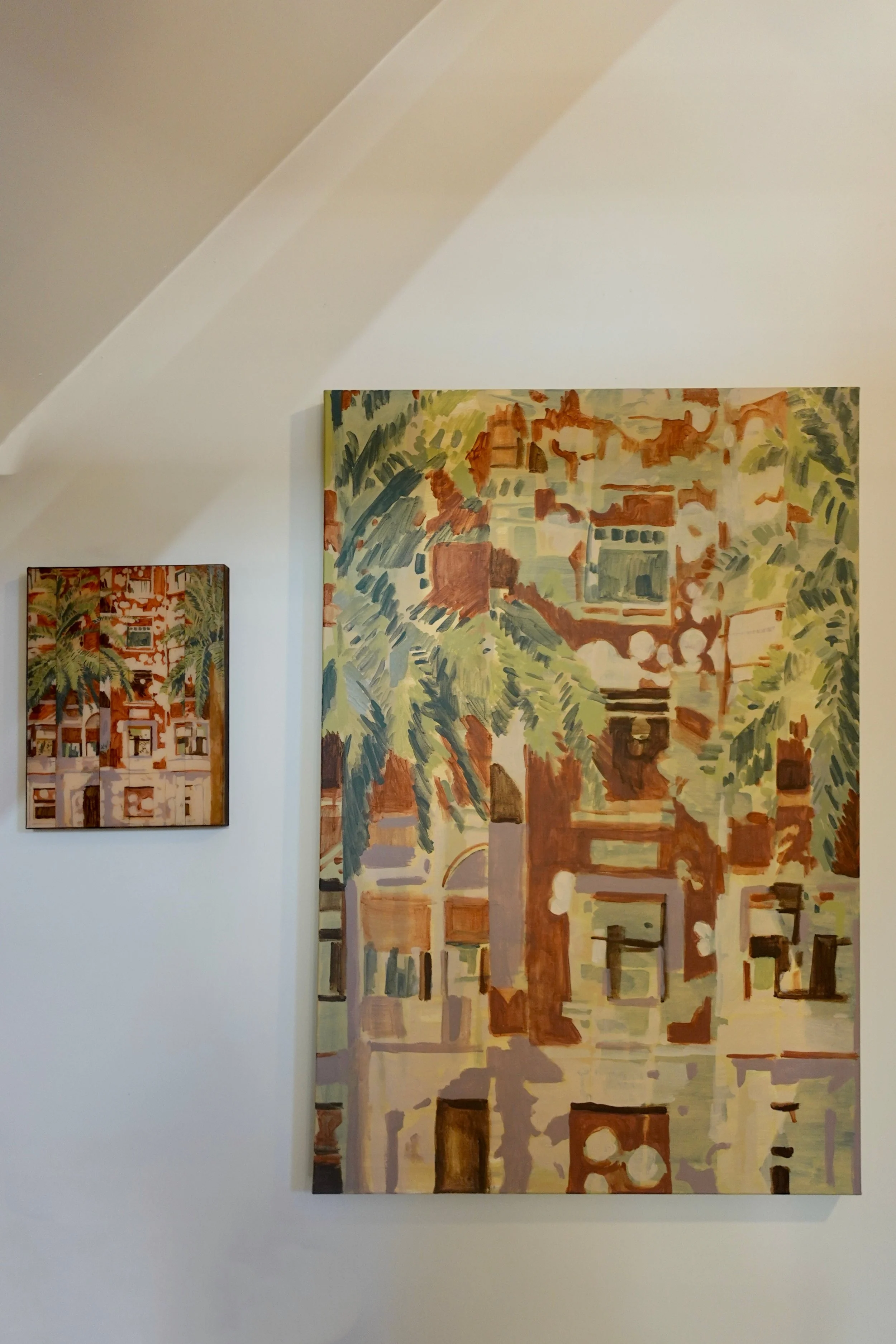 Two colorful abstract paintings on a white wall, featuring warm earthy tones and greenish hues, depicting cityscape and architectural elements.