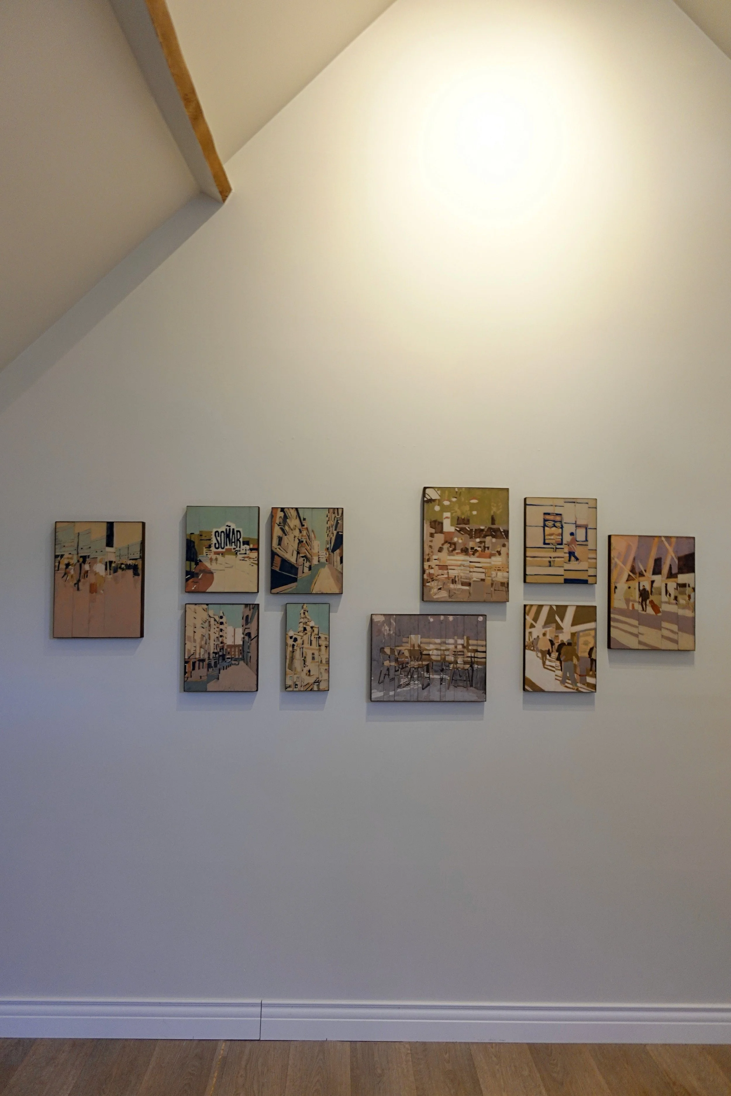 Gallery wall displaying framed artworks with various cityscape scenes and illustrations in the atelier.