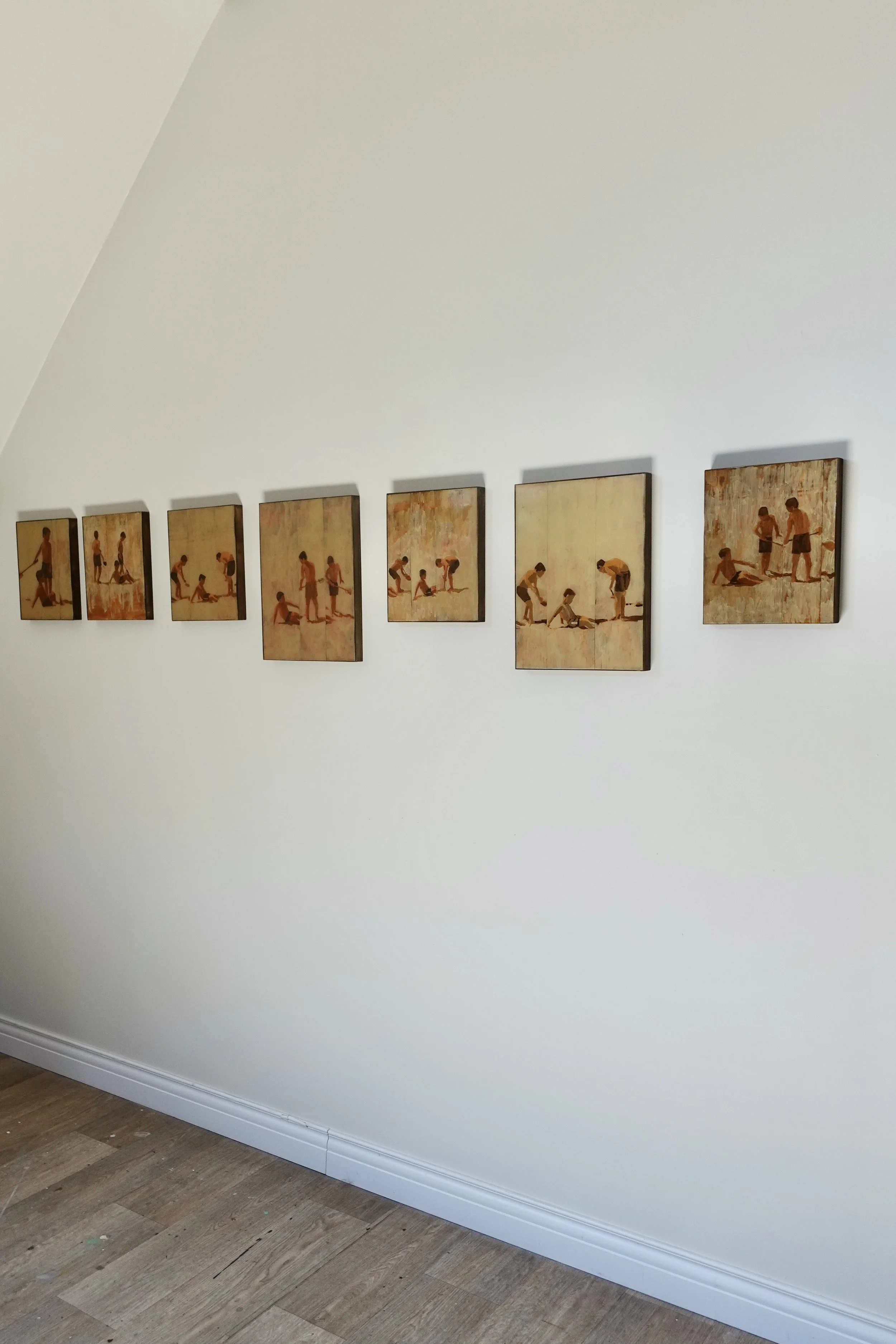 A row of eight small paintings depicting children playing on a wall in the studio The paintings show children playing a game  in the sand, covering one of the children with sand,  with a warm color palette and an impressionistic style.
