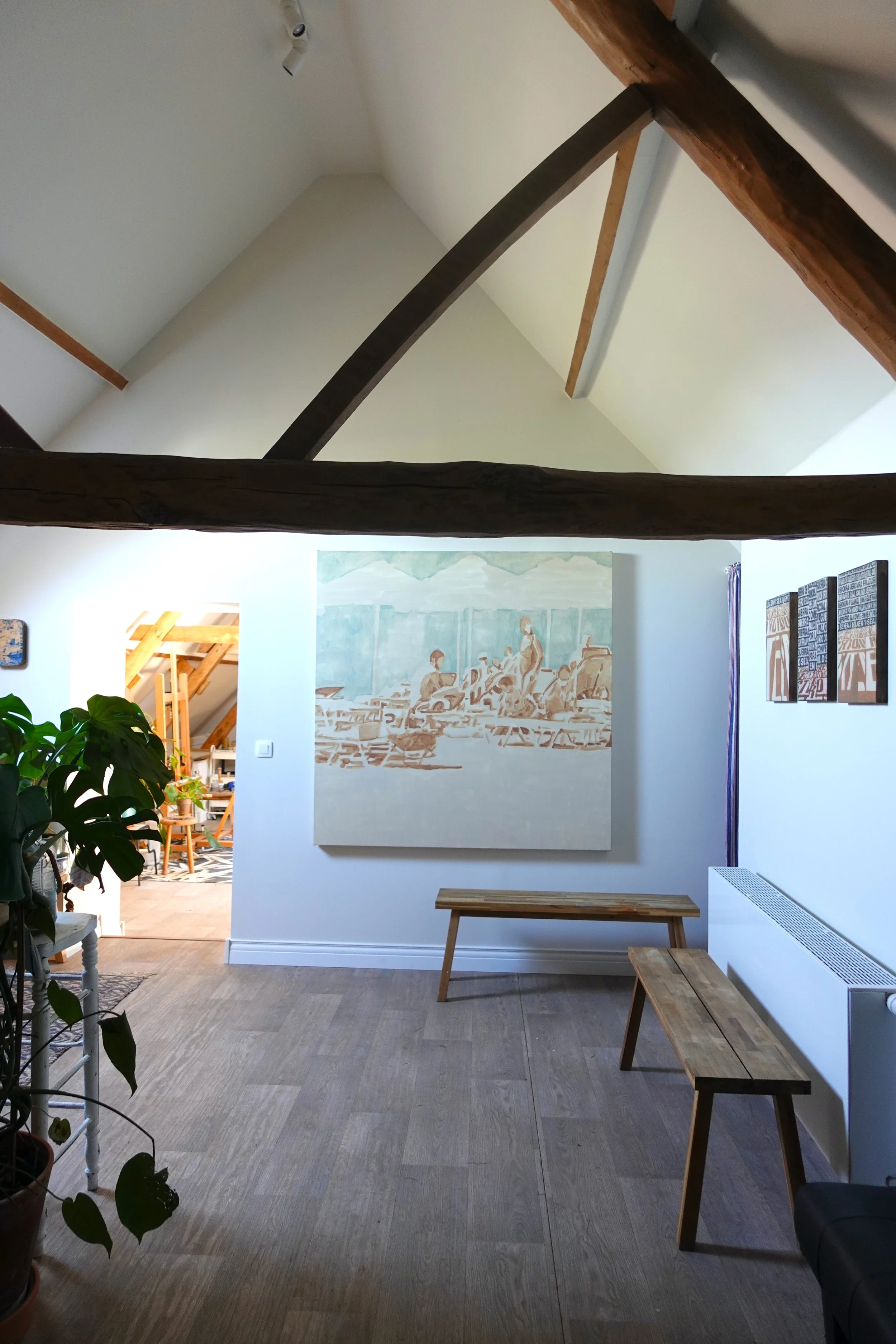 Living room with wooden benches, a large painting on the wall, and a plant on the left side.