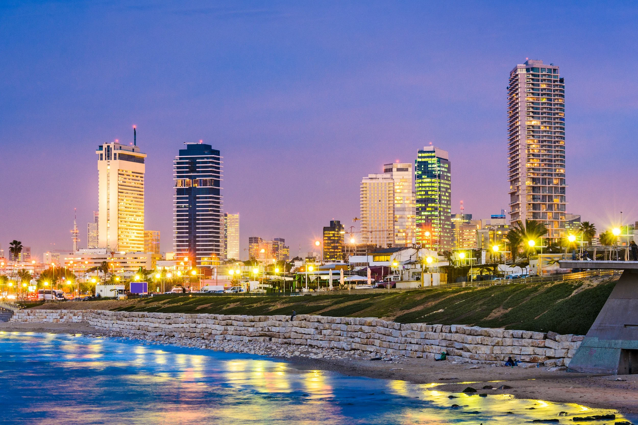 Tel Aviv skyline at dusk with lit buildings reflecting on the sea.