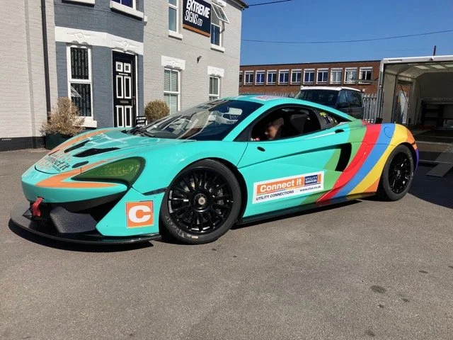 A colorful race car with sponsorship stickers parked outside buildings.