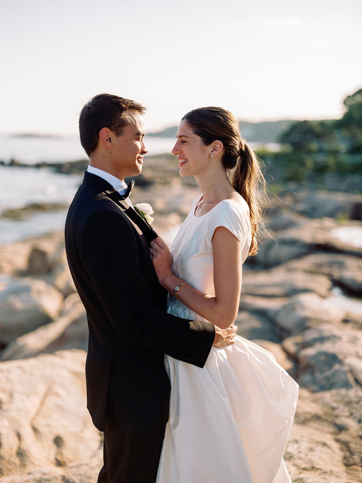 Elegant bride and groom standing together on a scenic shoreline at golden hour.