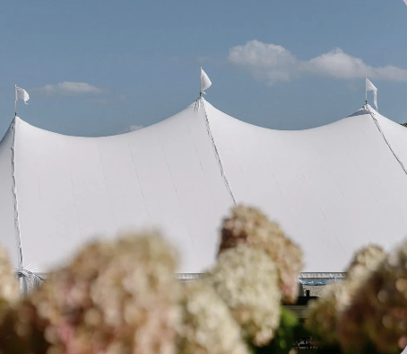 White sailcloth wedding tent framed by blooming hydrangeas, showcasing an elegant outdoor reception setting on a clear summer day.