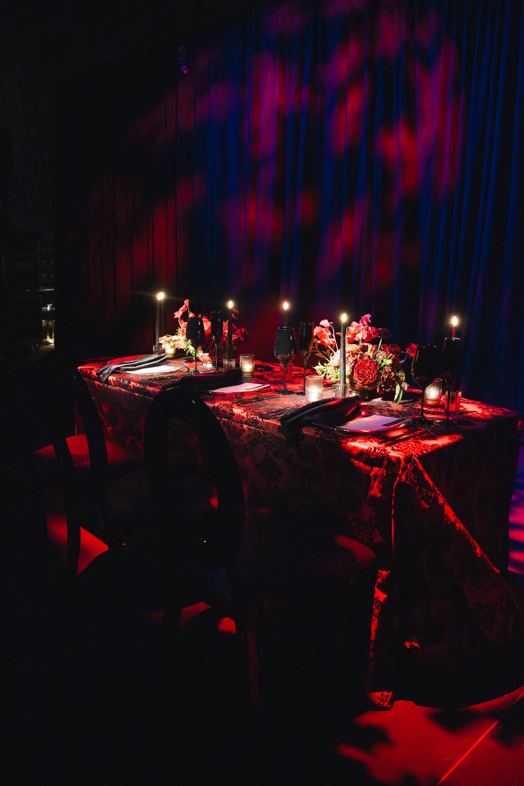 Decorated event tent with floral arrangements on wooden support beams, round tables with floral centerpieces, and black chairs on a grassy outdoor setting.