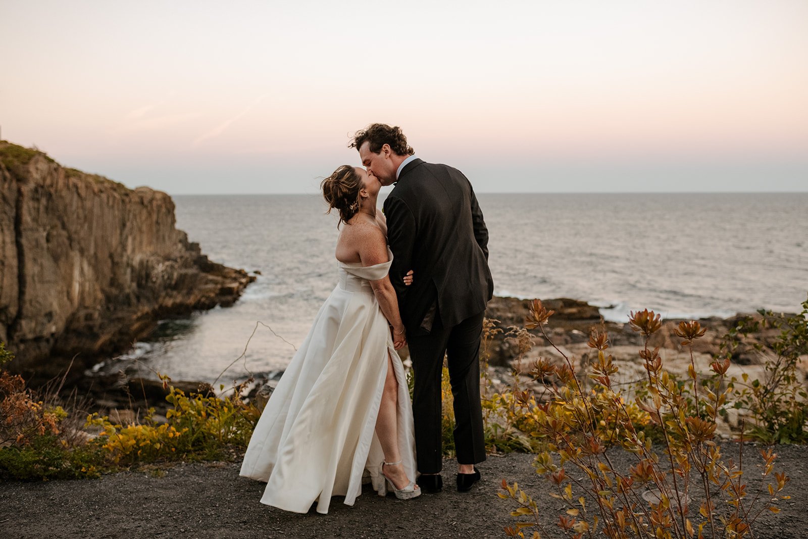 Newlyweds kiss overlooking the ocean during their coastal wedding planned with full-service wedding planning support.