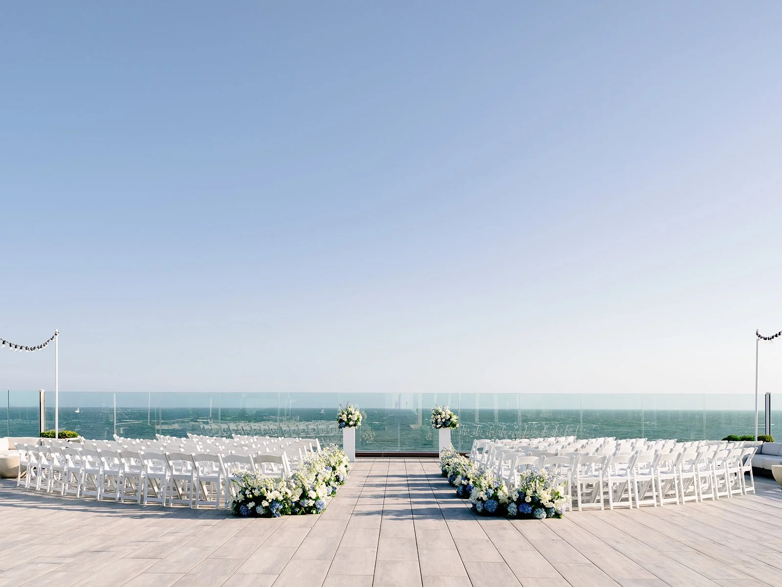 Wychmere Beach Club oceanfront ceremony setup with white chairs, floral-lined aisle, and sea views.