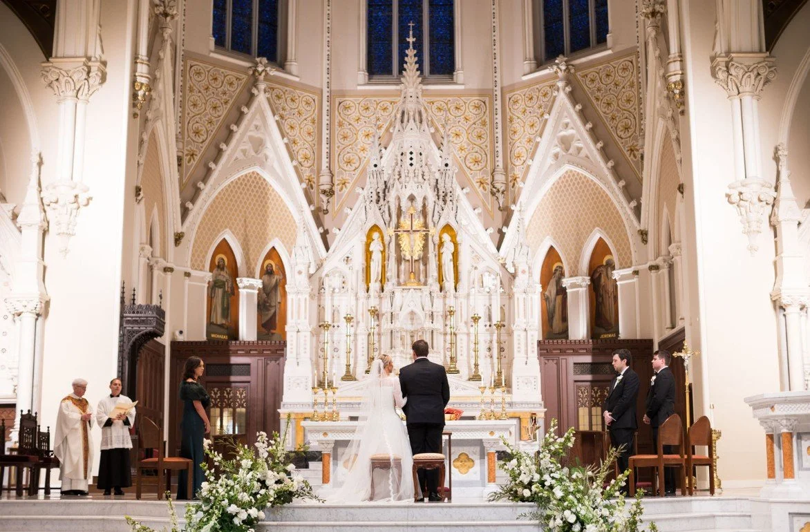 A couple getting married at an ornate church altar with priests and attendants present.