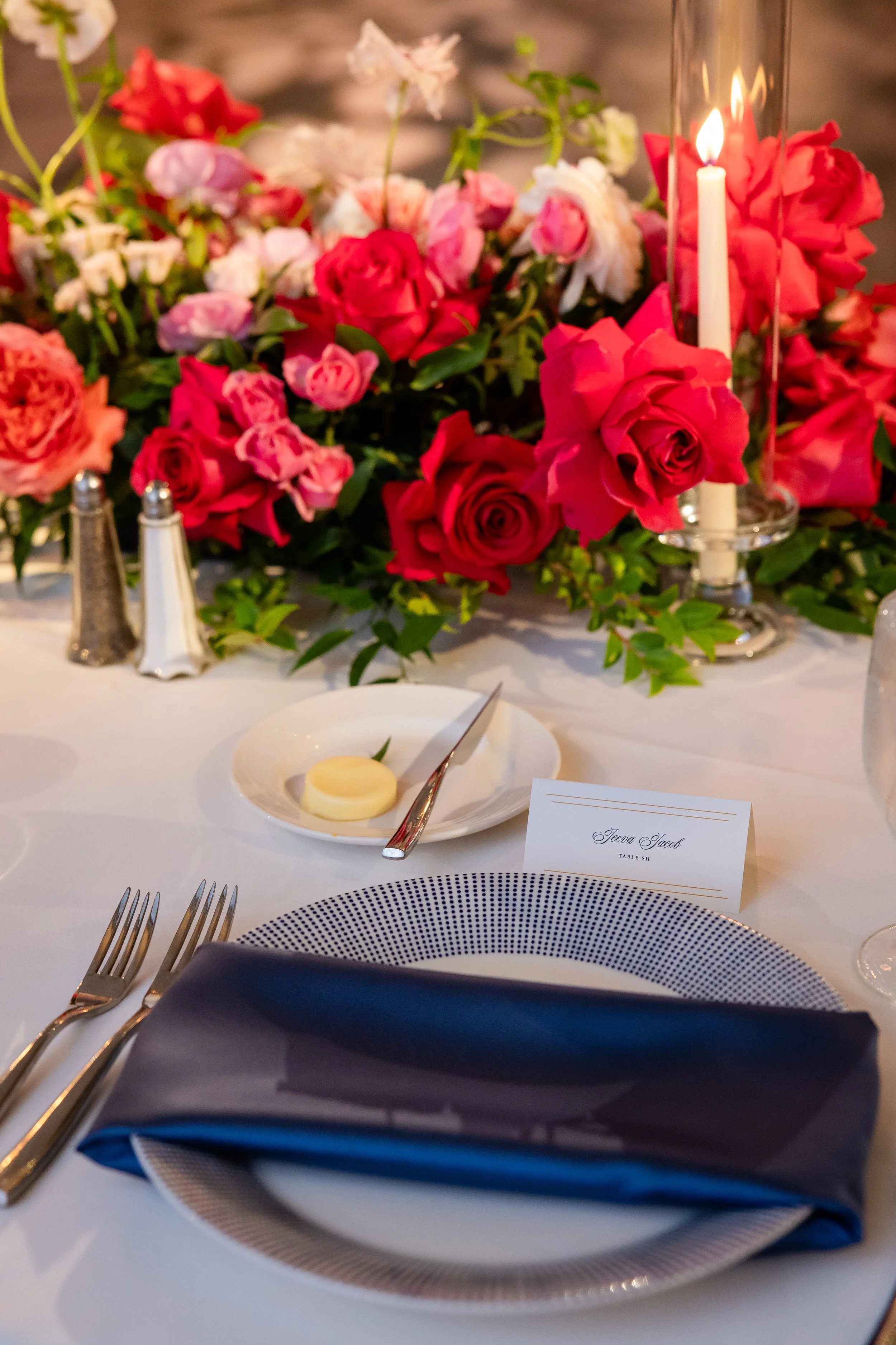A large yellow house with a porch on a lawn with several people gathered, some standing and some seated, with a tent set up nearby for an outdoor event, and trees in the background.
