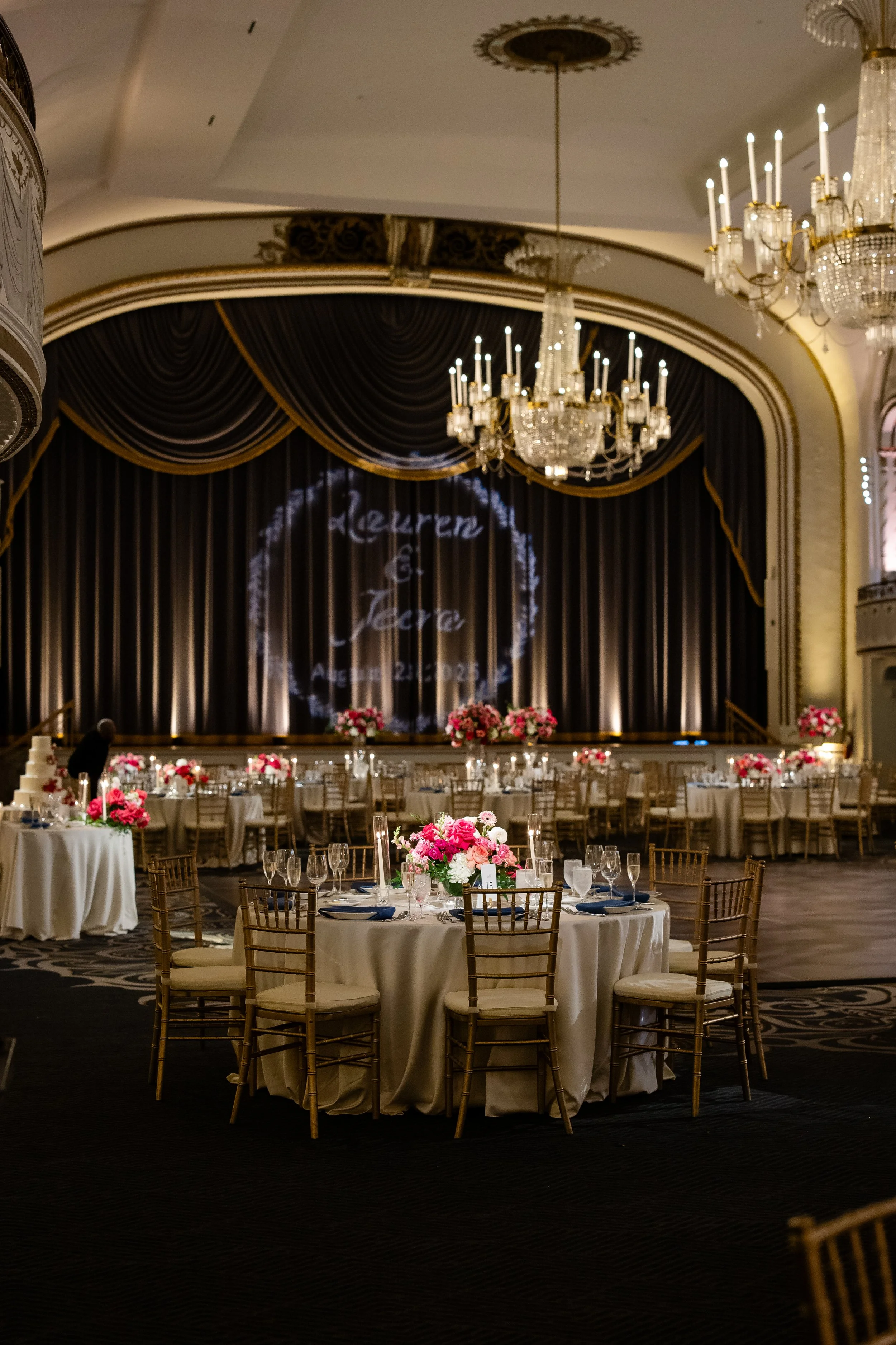 Elegant outdoor dining table decorated with a pink and red floral centerpiece, surrounded by glassware, plates, and silverware, set in a garden.