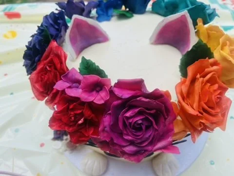 Cake decorated with colorful flowers and unicorn ears, resembling a unicorn-themed cake.