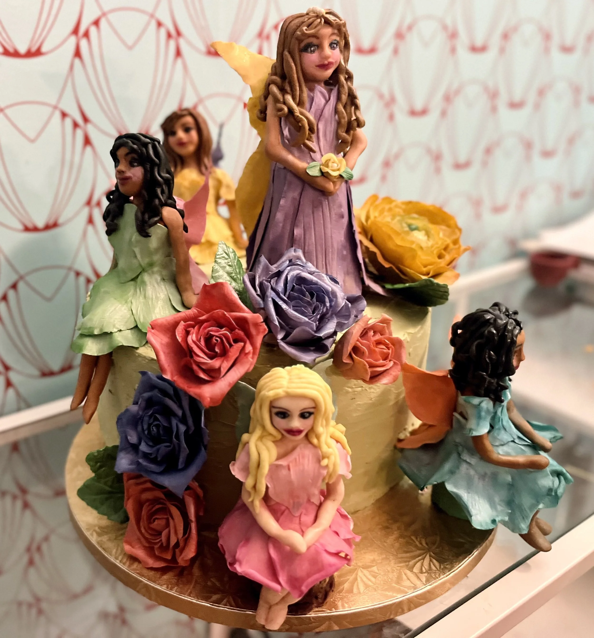 A decorative cake with figurines of fairies and colorful roses on top.