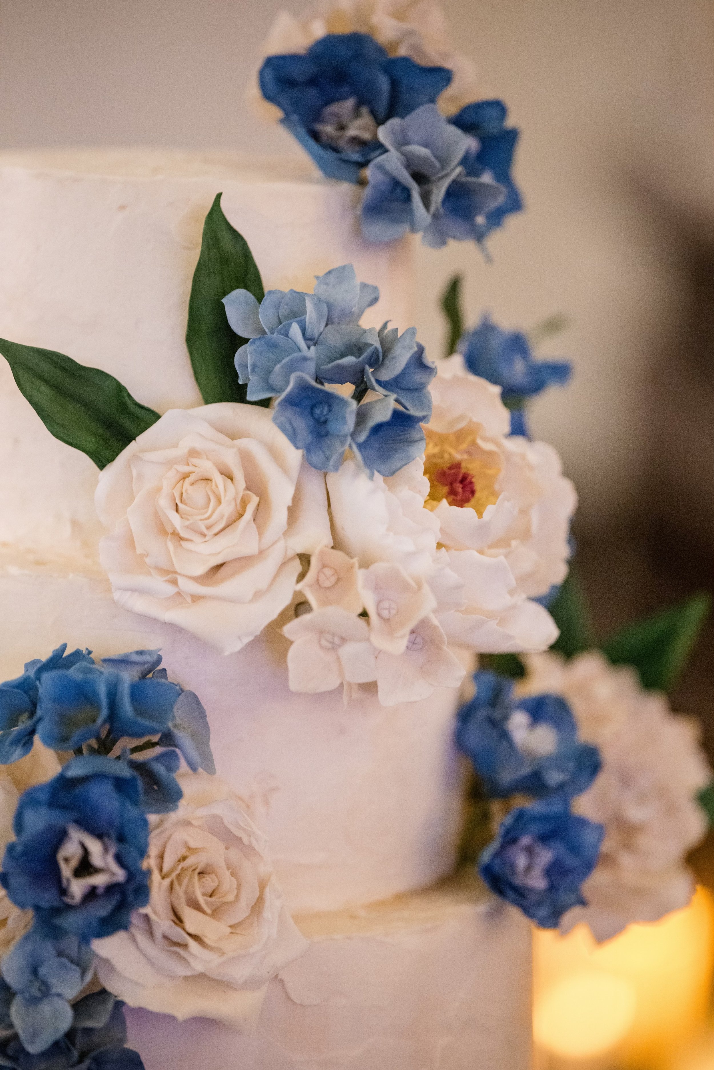 Close-up of a wedding cake decorated with white and blue flowers, including roses and hydrangeas.