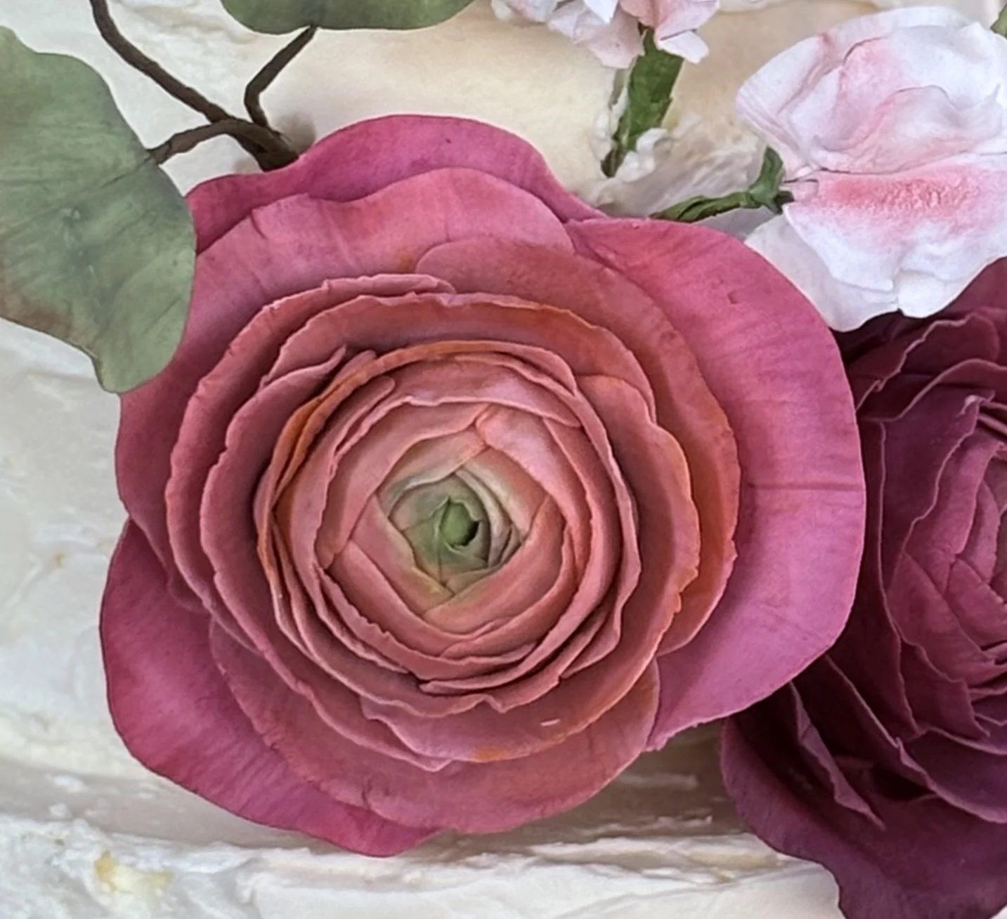 Close-up of a pink ranunculus flower with layered petals, surrounded by other pink and white flowers and green leaves.