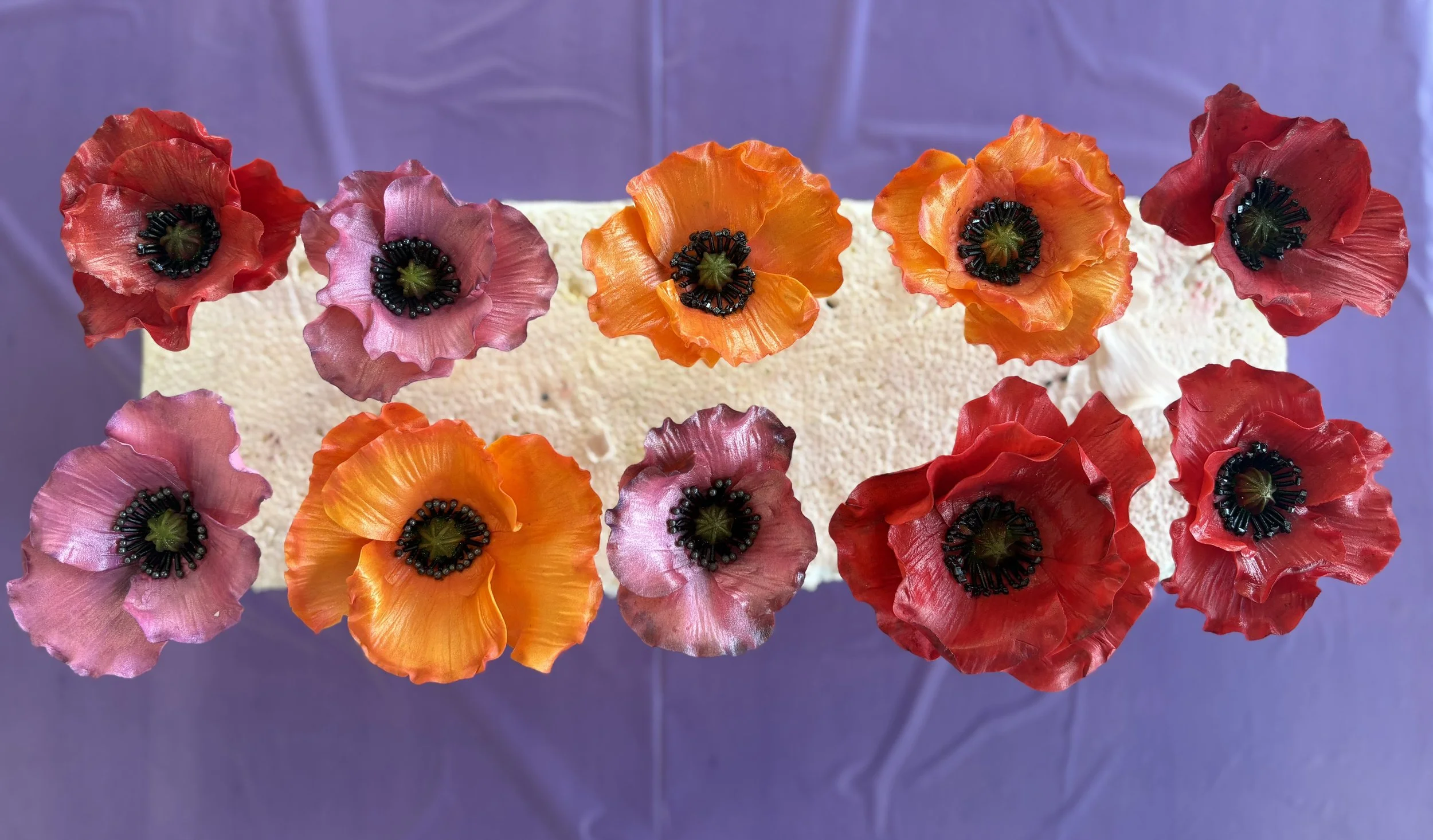 Cake decorated with edible poppy flower toppers in red, pink, orange, and purple colors.