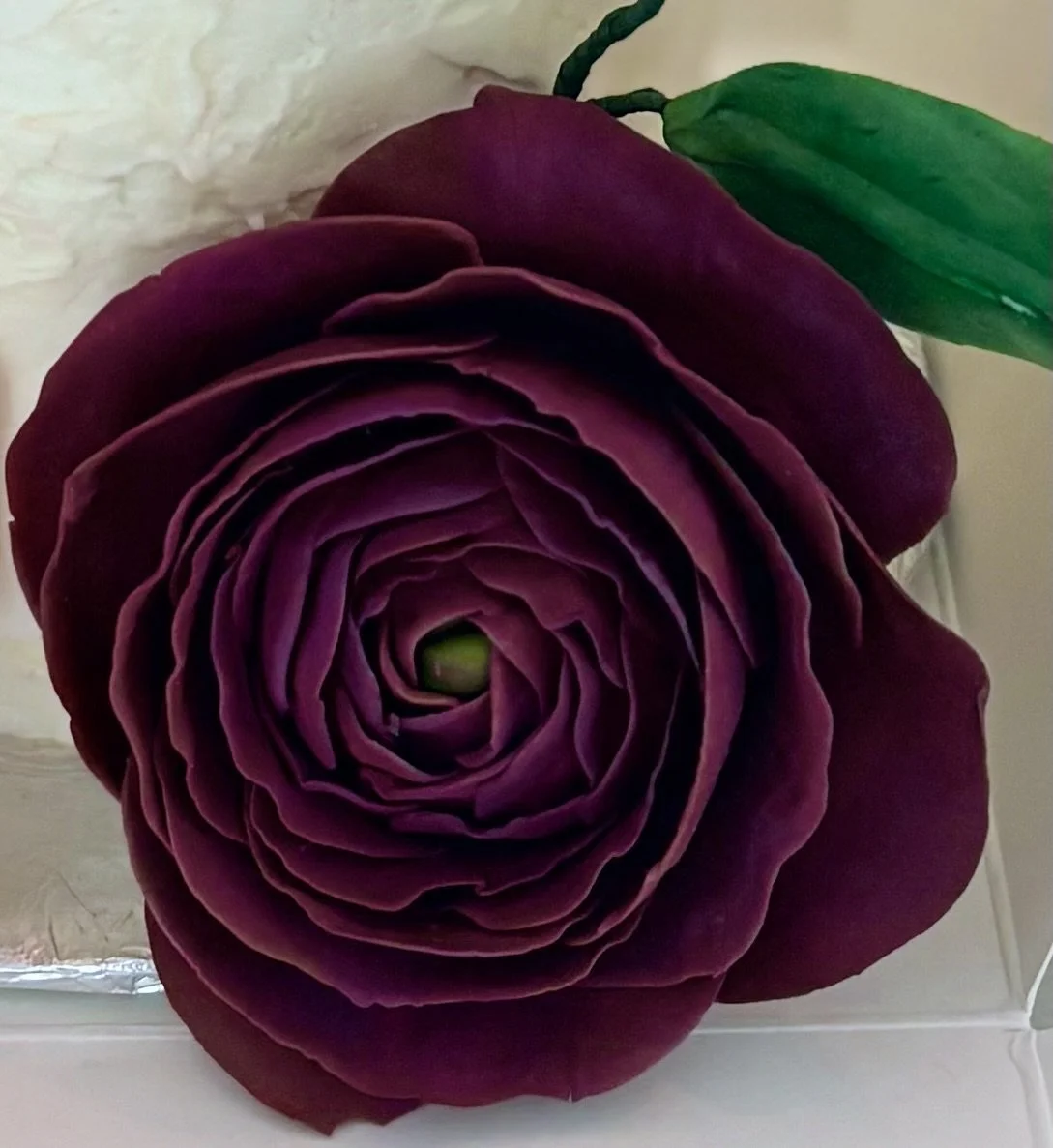 Close-up of a deep red artificial rose with layered petals and a green leaf attached.