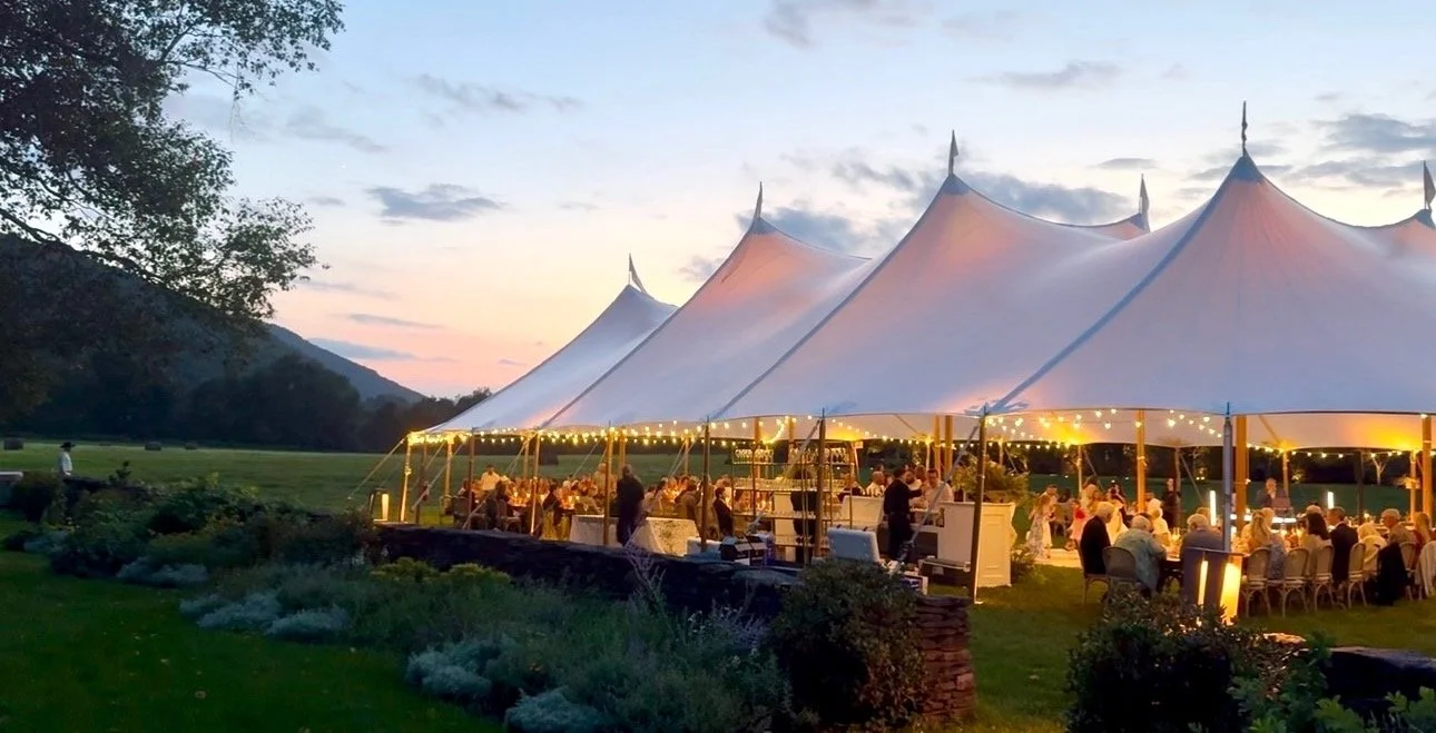 Sailcloth tents lit from within at dusk, the mountain behind the field